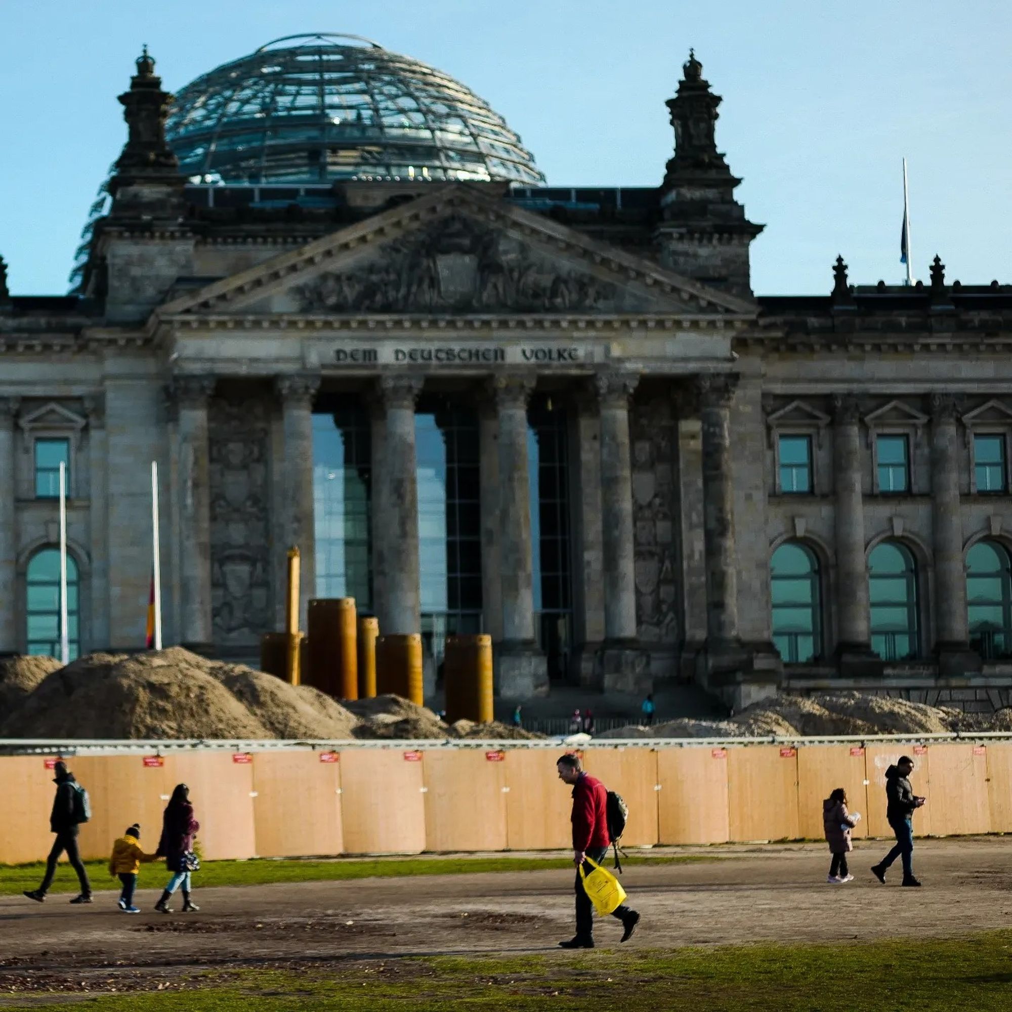 Reichstag Berlin  davor eine Baustelle, Menschen, ein Mensch mit roter Jacke und gelber Tüte