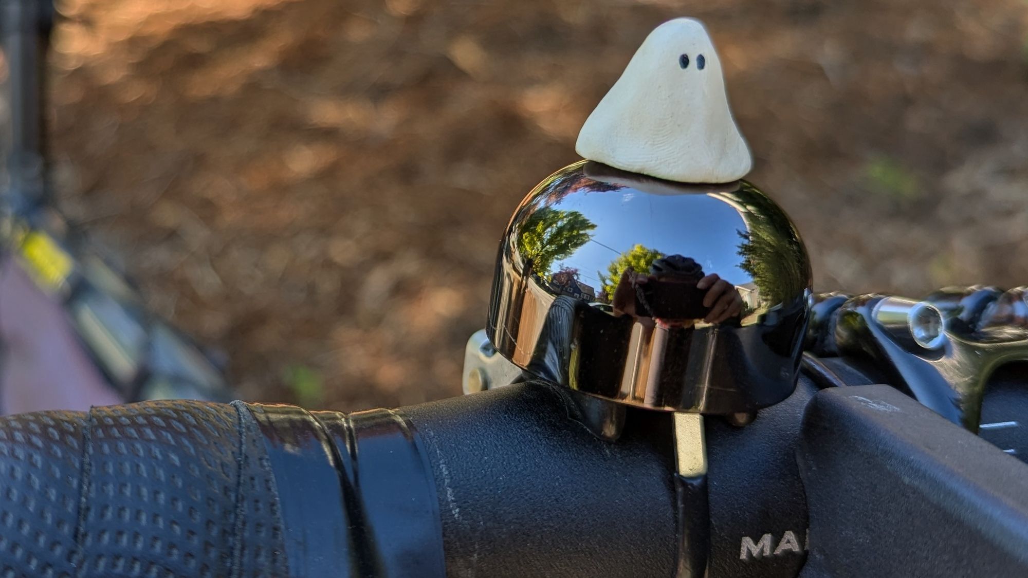 A little ghost figurine sitting atop a shiny black bell on the handlebars of my bike