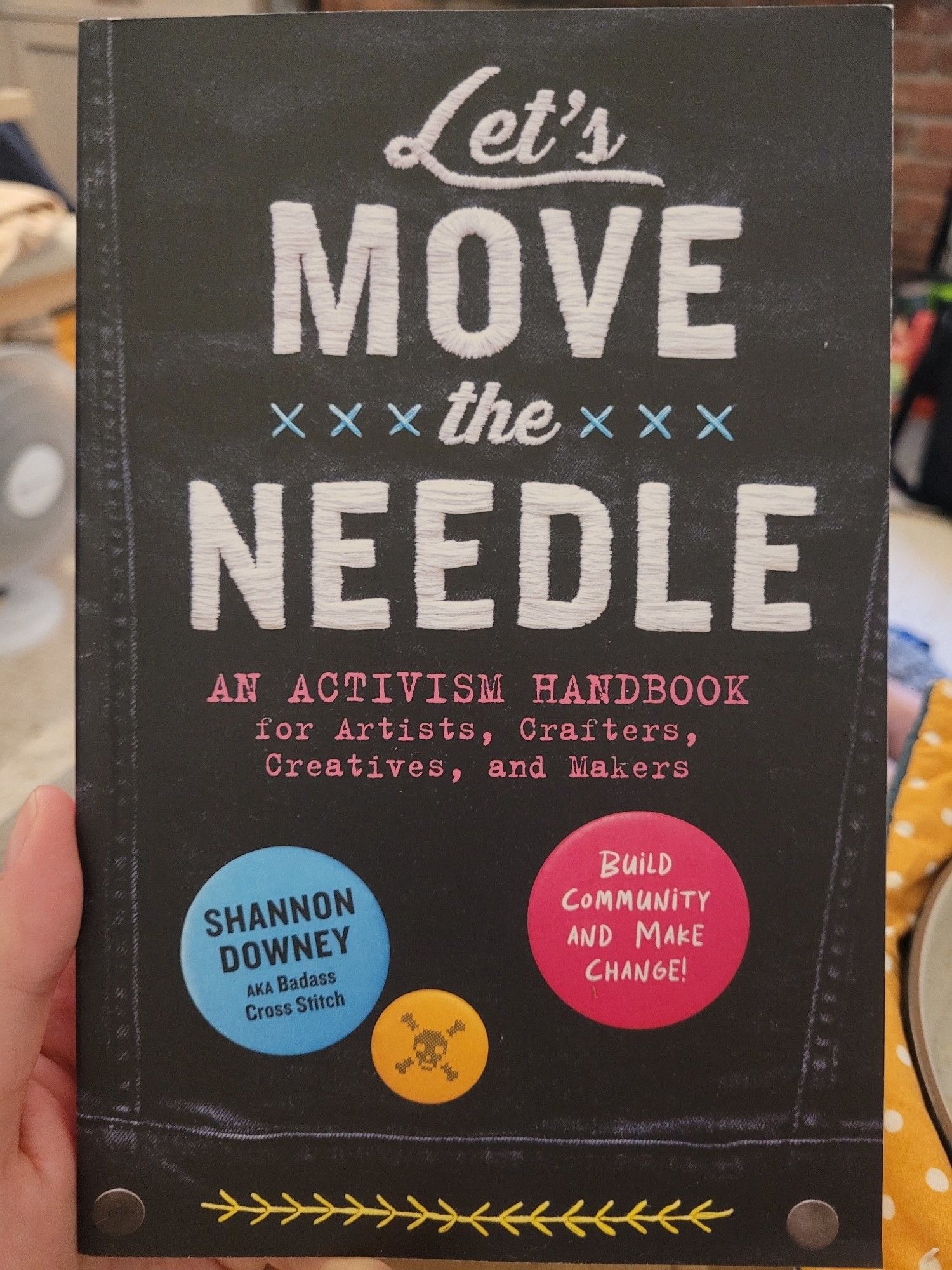 Book cover of "Let's move the needle: an activism handbook for artists, crafters, creatives, and makers" 

The cover looks like the back of a denim jacket, with the text in an embroidery style and blurbs that look like buttons. It's very punk.