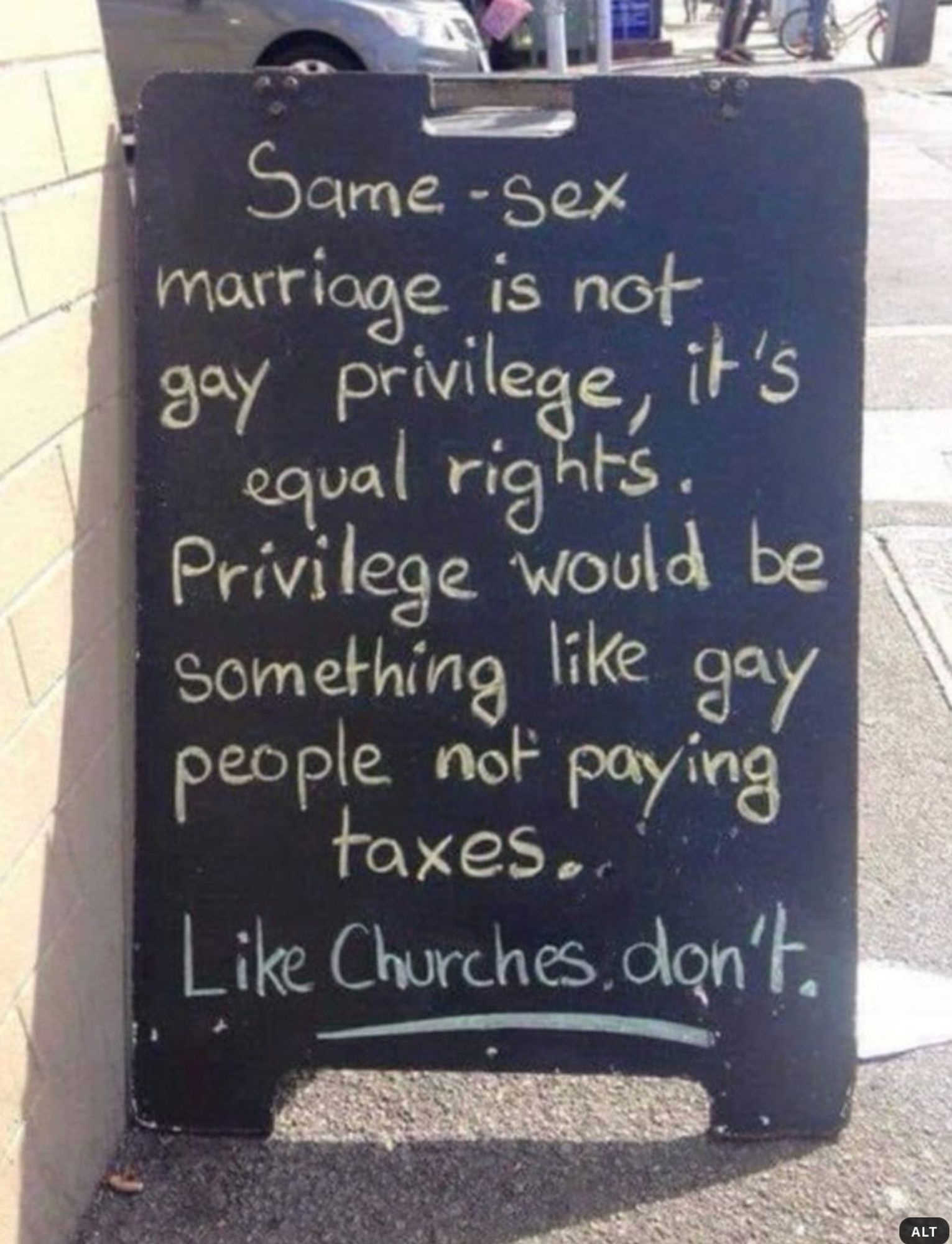 A portable sandwich-sign outside a building on a sidewalk on a sunny day with a chalked message that reads:
"Same-sex marriage is not gay privilege, it's civil rights. Privilege would be something like gay people not paying taxes. -- Like churches don't."