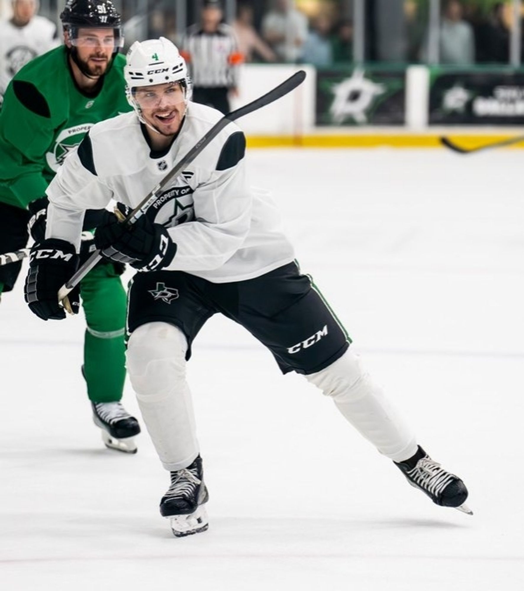 Miro Heiskanen and Tyler Seguin of the Dallas Stars skating at practice. They are wearing solid green and solid white jerseys with black accents at the shoulders that look like missing fabric cutouts.