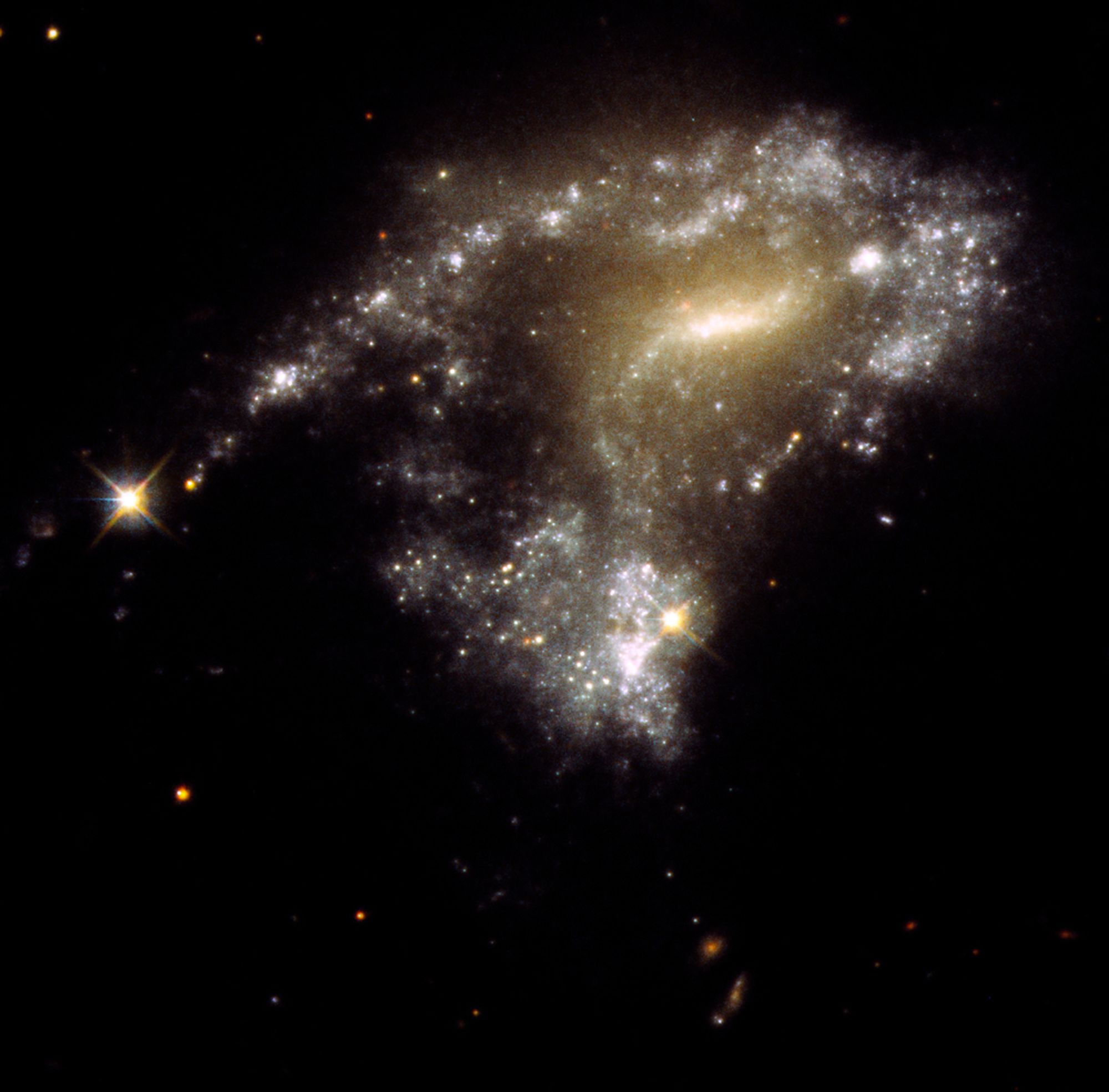 This is a picture of a galaxy with a peculiar S-shape. It has a bright milky-white core at the center. Twin arms of blue stars wrap around the core. One arm looks particularly stretched out due to the gravitational tidal pull of a neighboring galaxy. Bright, young, whitish star clusters are strung along the arm like a string of pearls. They formed as a result of the collision process.