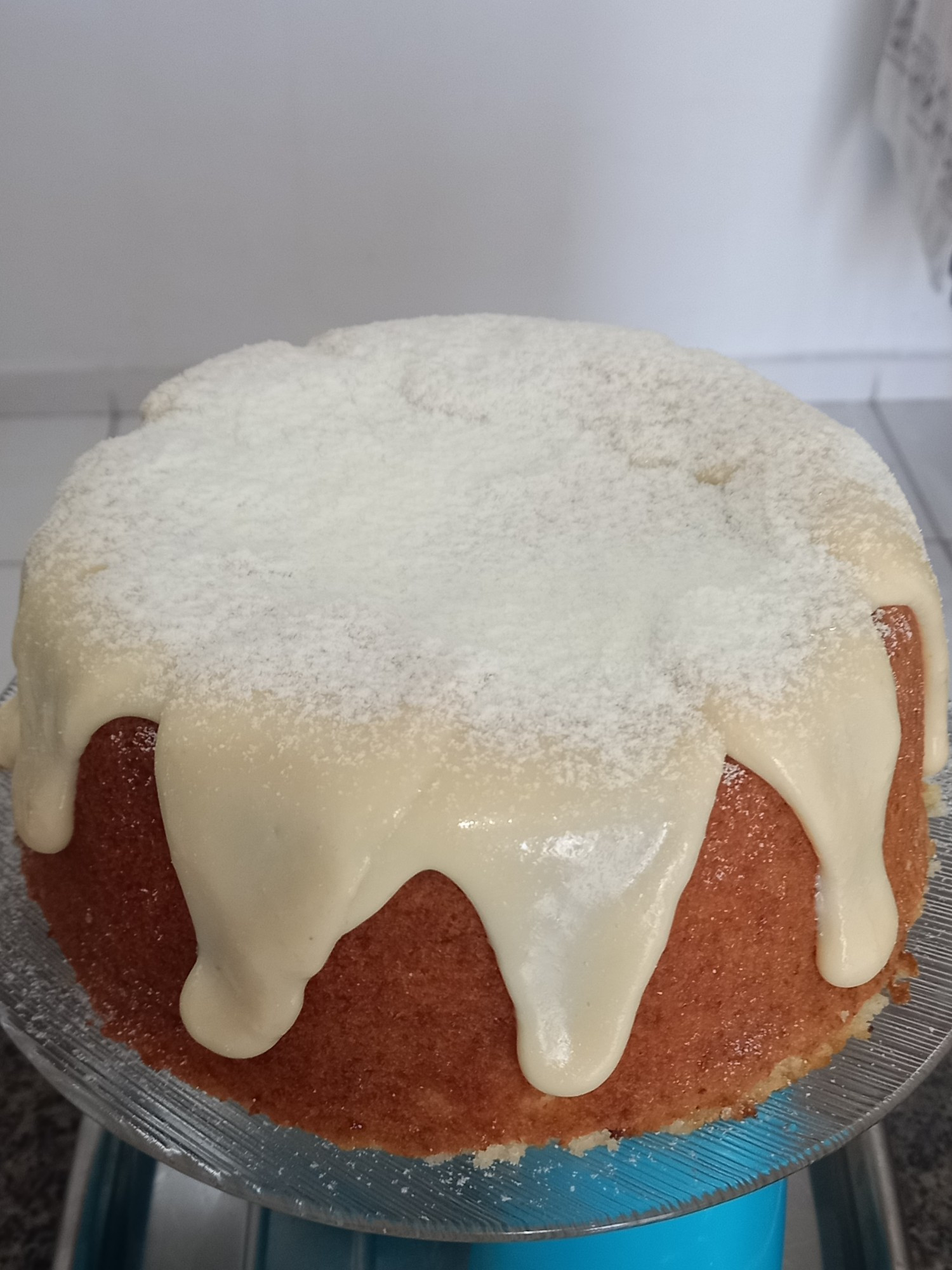 Foto de um bolo de leite coberto com brigadeiro branco e leite em pó salpicado por cima da cobertura. 