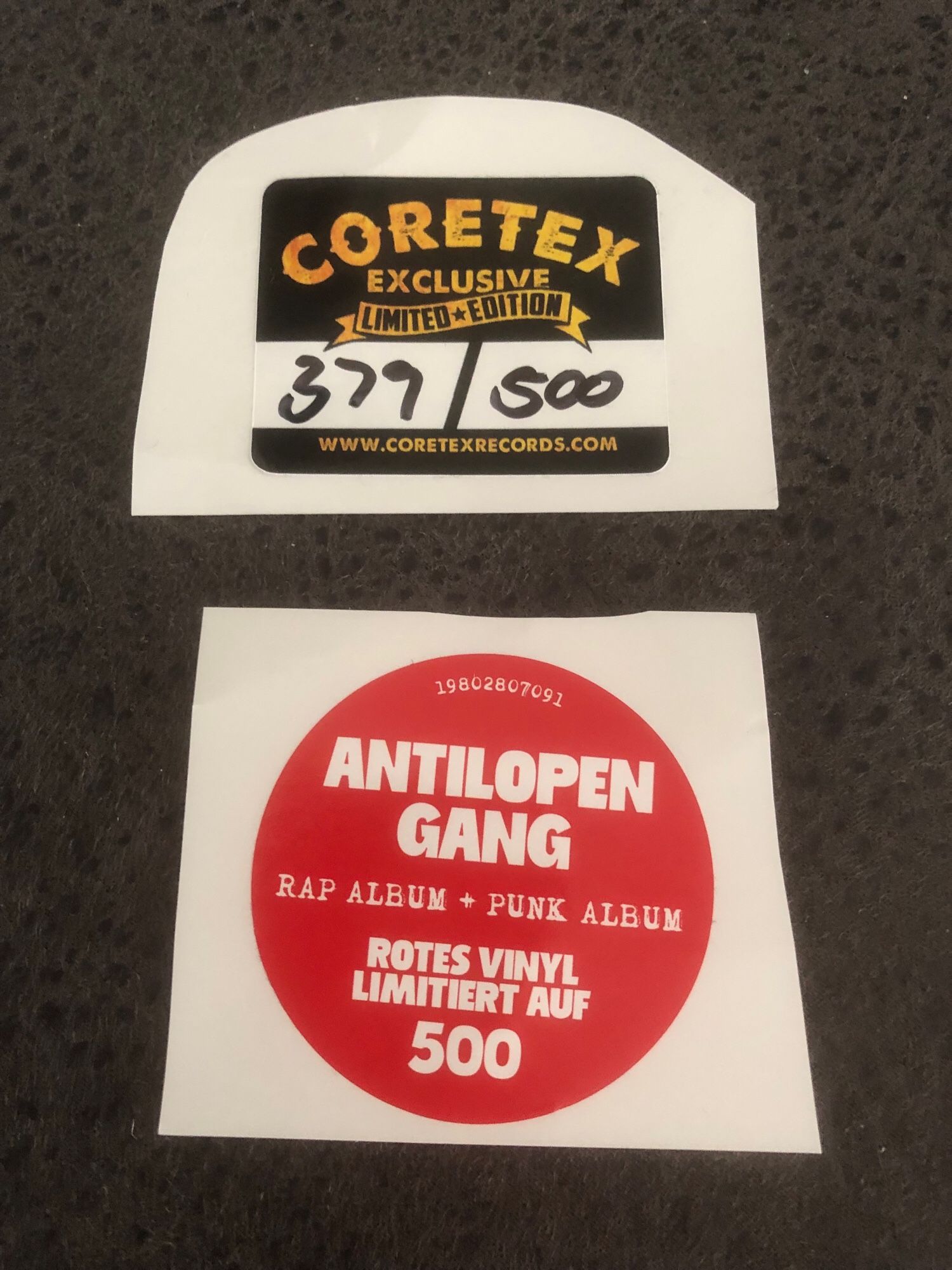 Die beiden Sticker auf der Folie (der erste wurde bereits beschrieben) des Albums. Der zweite Sticker ist rund mit der Grundfarbe rot und weißer Schrift: „Antilopengang Rap Album + Punk Album Rotes Vinyl Limitiert auf 500“