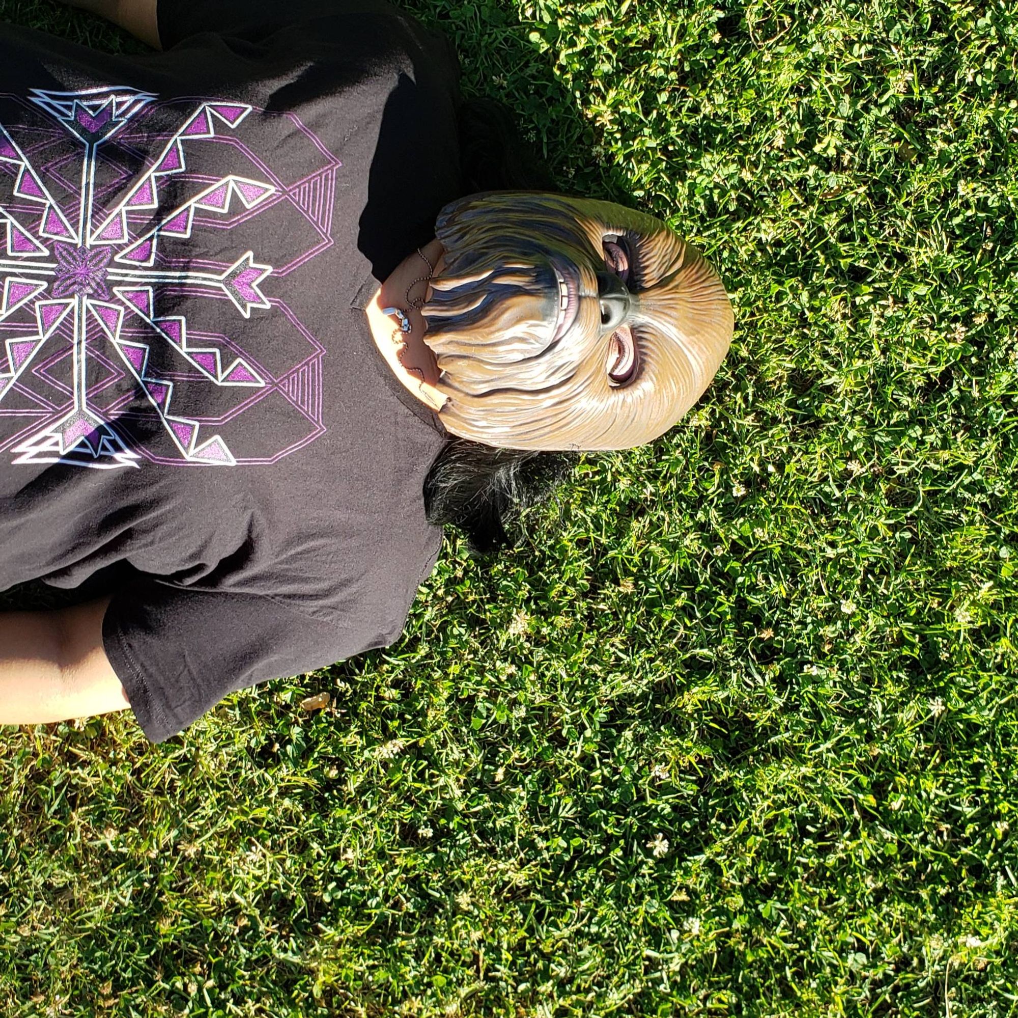 A photo of johnnie jae laying on the ground with her arms by her side and wearing a wookie mask