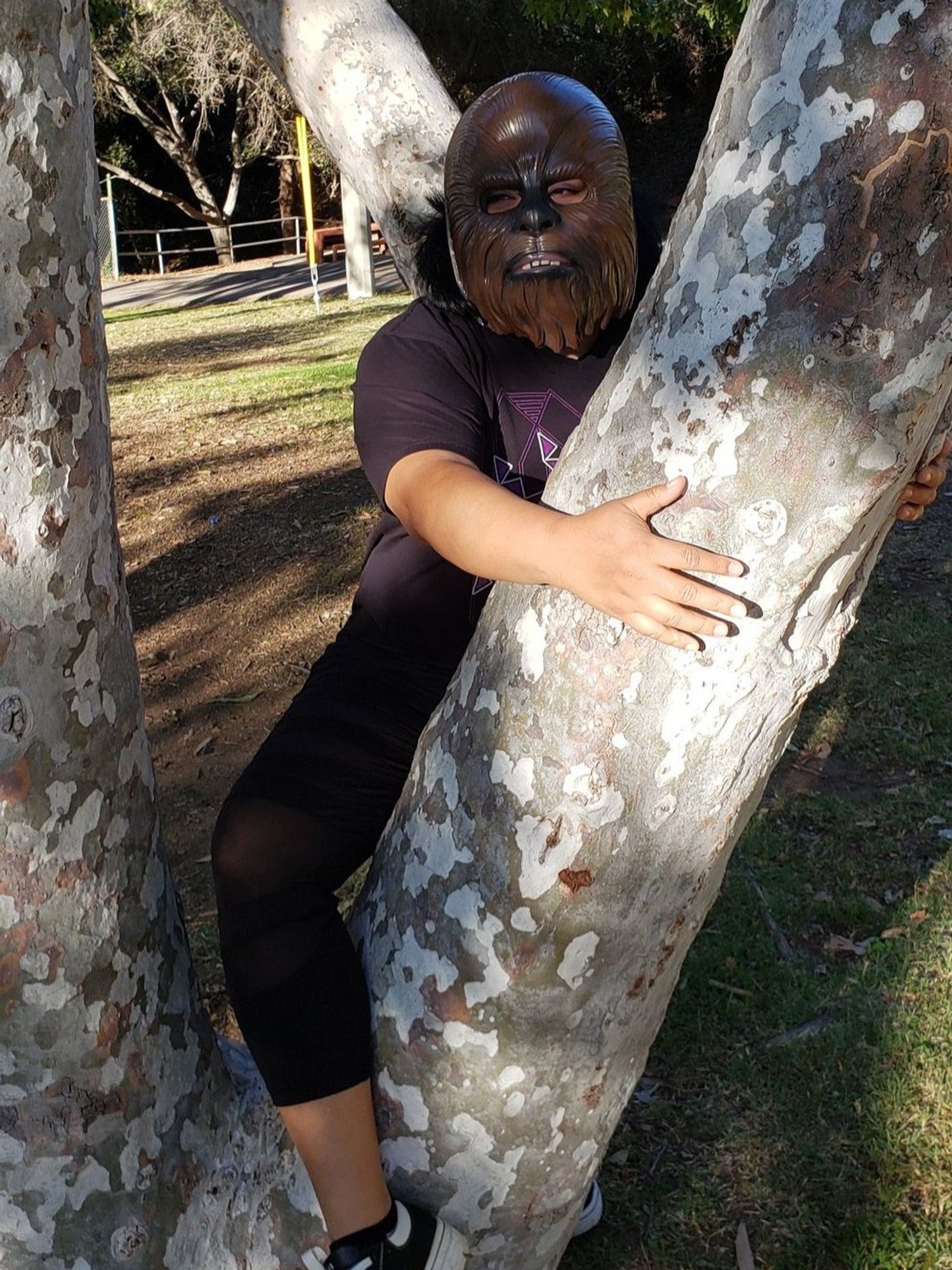 Johnnie Jae hugging a tree trunk like a stripper pole while wearing a wookie mask.