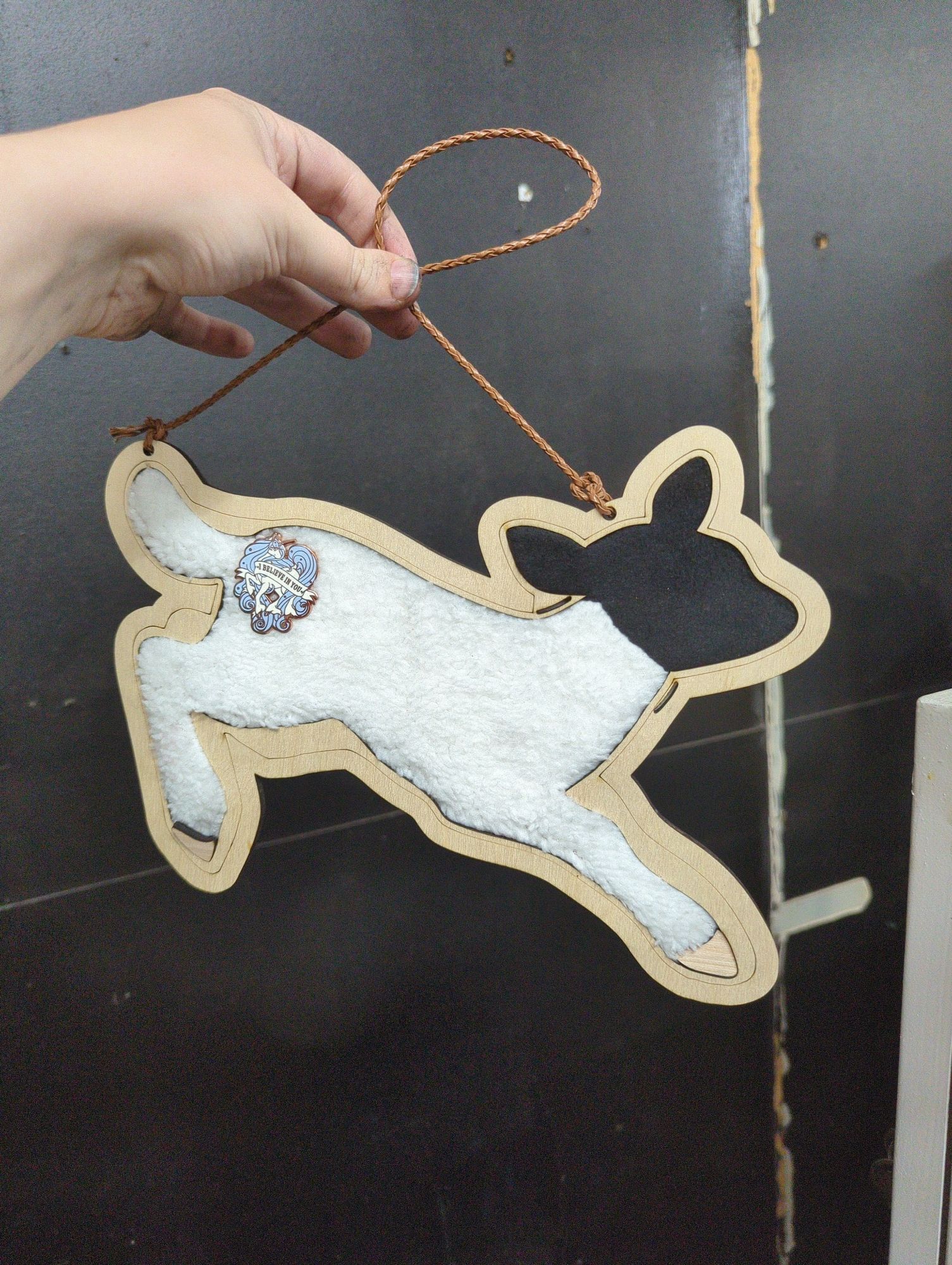 A wooden and fabric enamel pin board shaped like a black and white lamb