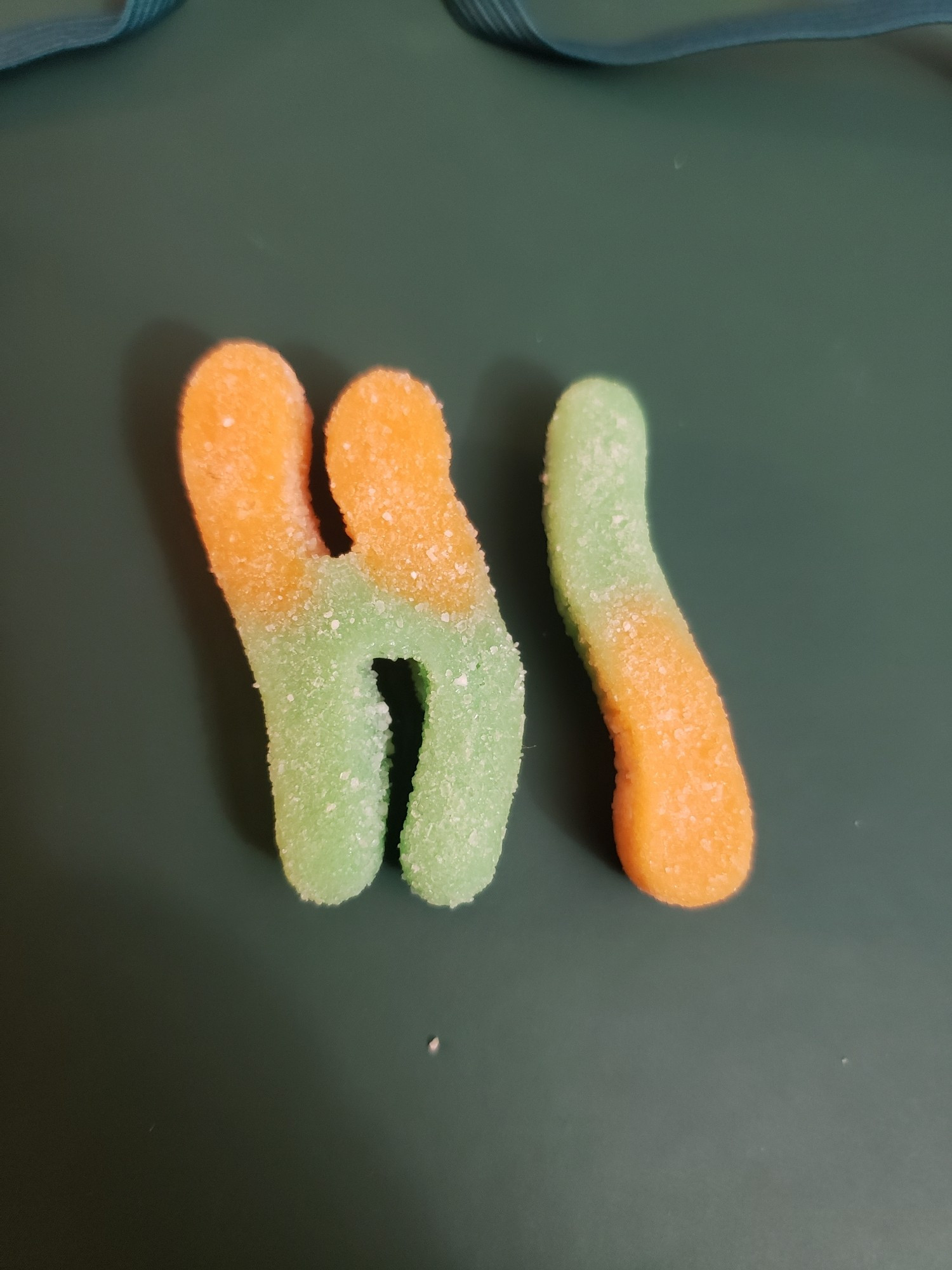 Two orange and green gummy worms. One is in the shape of an H and they say 'HI'