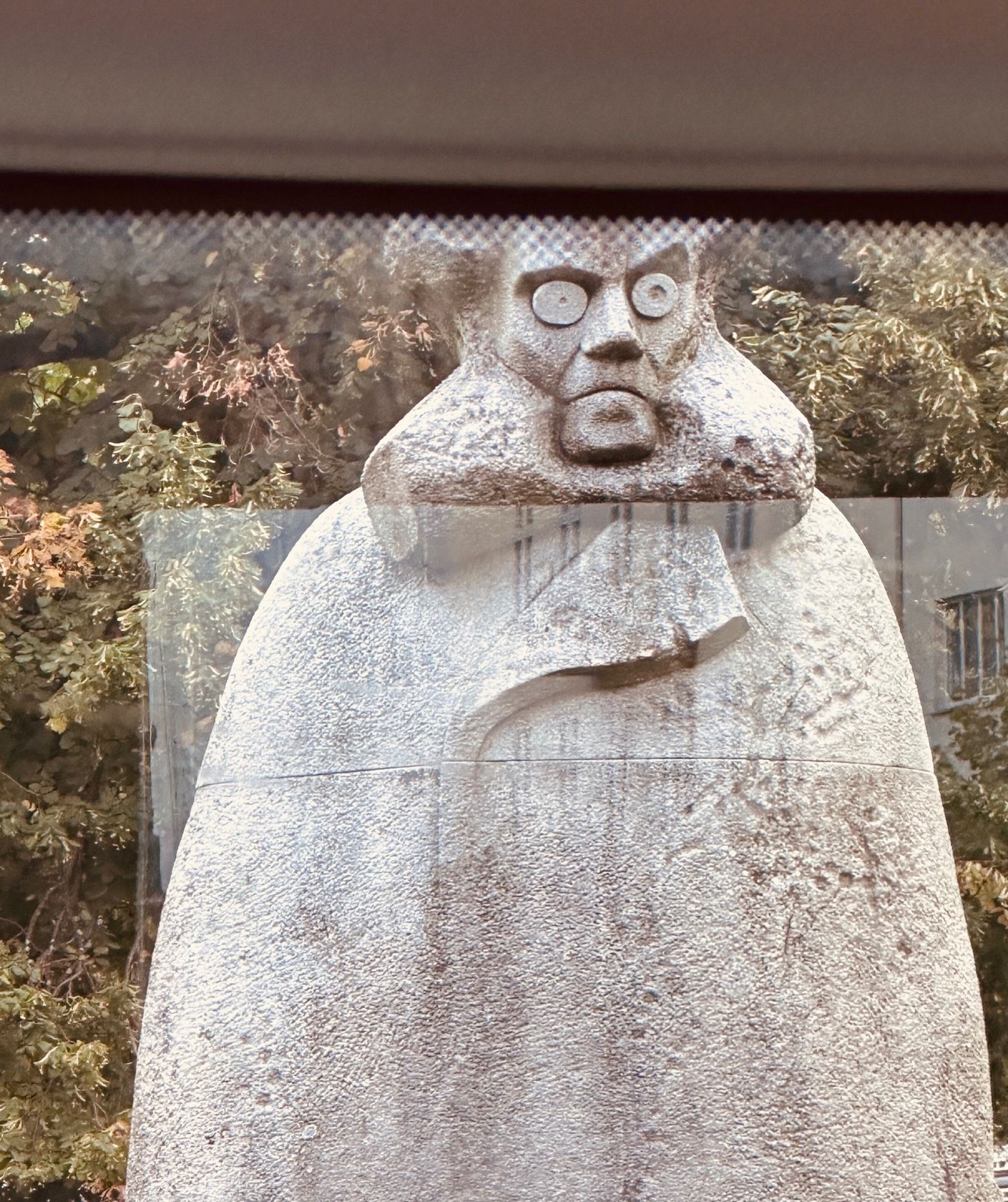 Grim-faced statue of Henrik Ibsen seen it through a bus window.