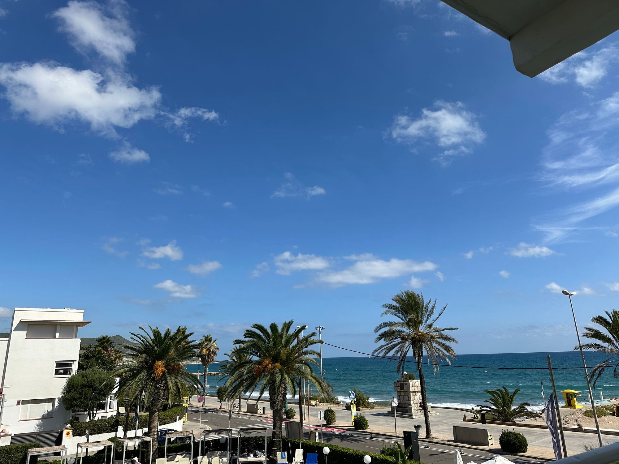 Blue sky over Mediterranean Sea. There are palm trees and a small road in the foreground. The hotel pool is just out of the bottom of the shot. 