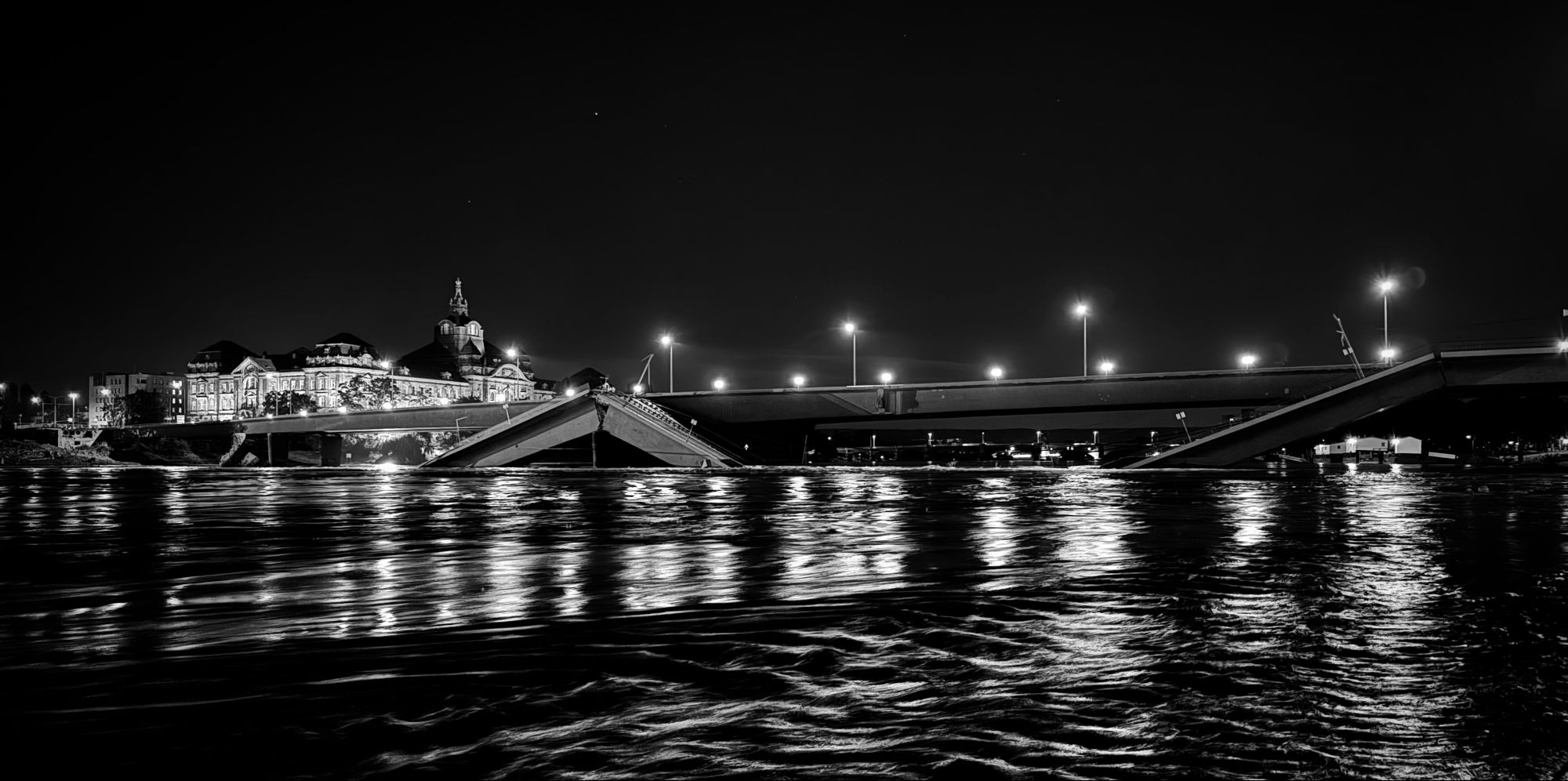 Blick auf die eingestürzte Carolabrücke in schwarz-weiß, vorne die hoch stehende Elbe