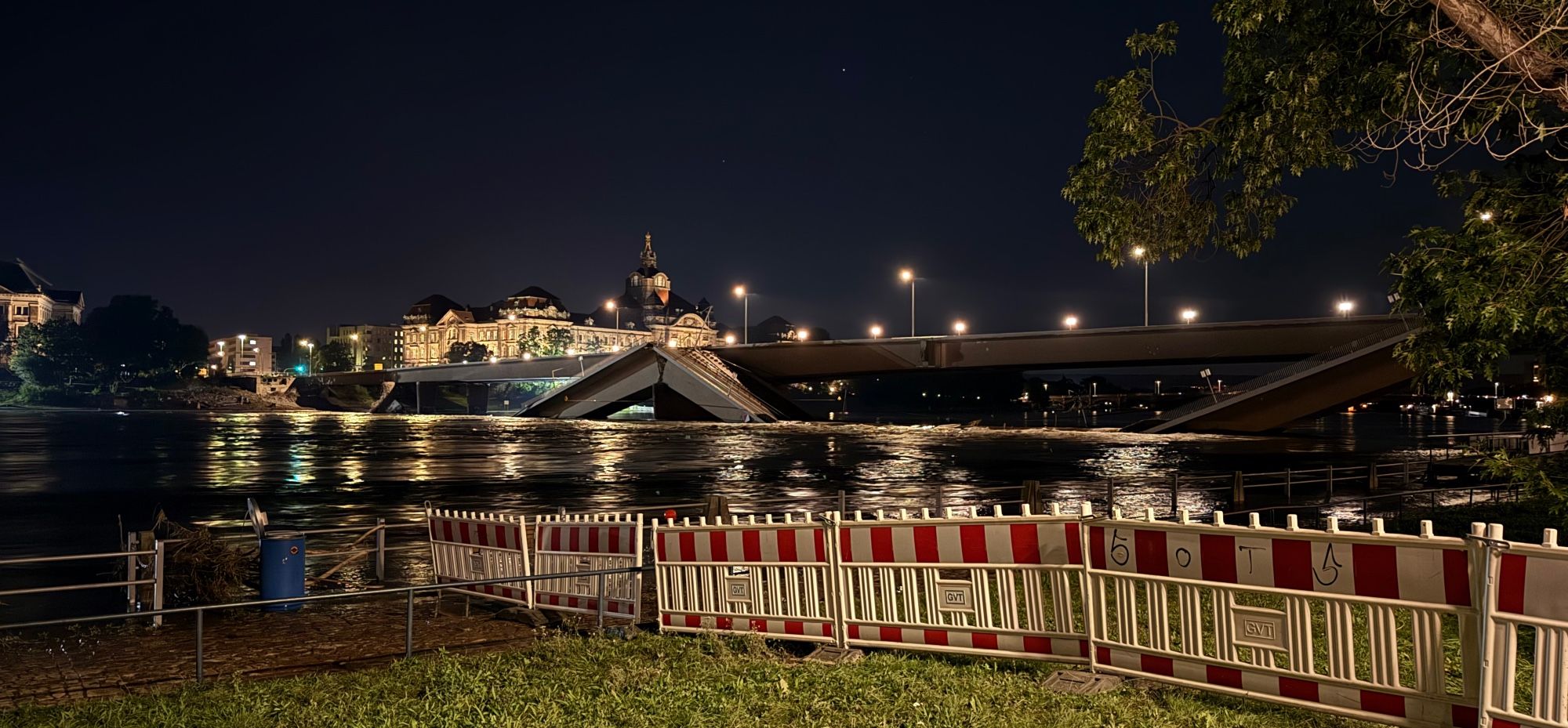 Blick auf die eingestürzte Carolabrücke im Abendlicht, vorne ein rot-weißer Bauzaun als Absperrung