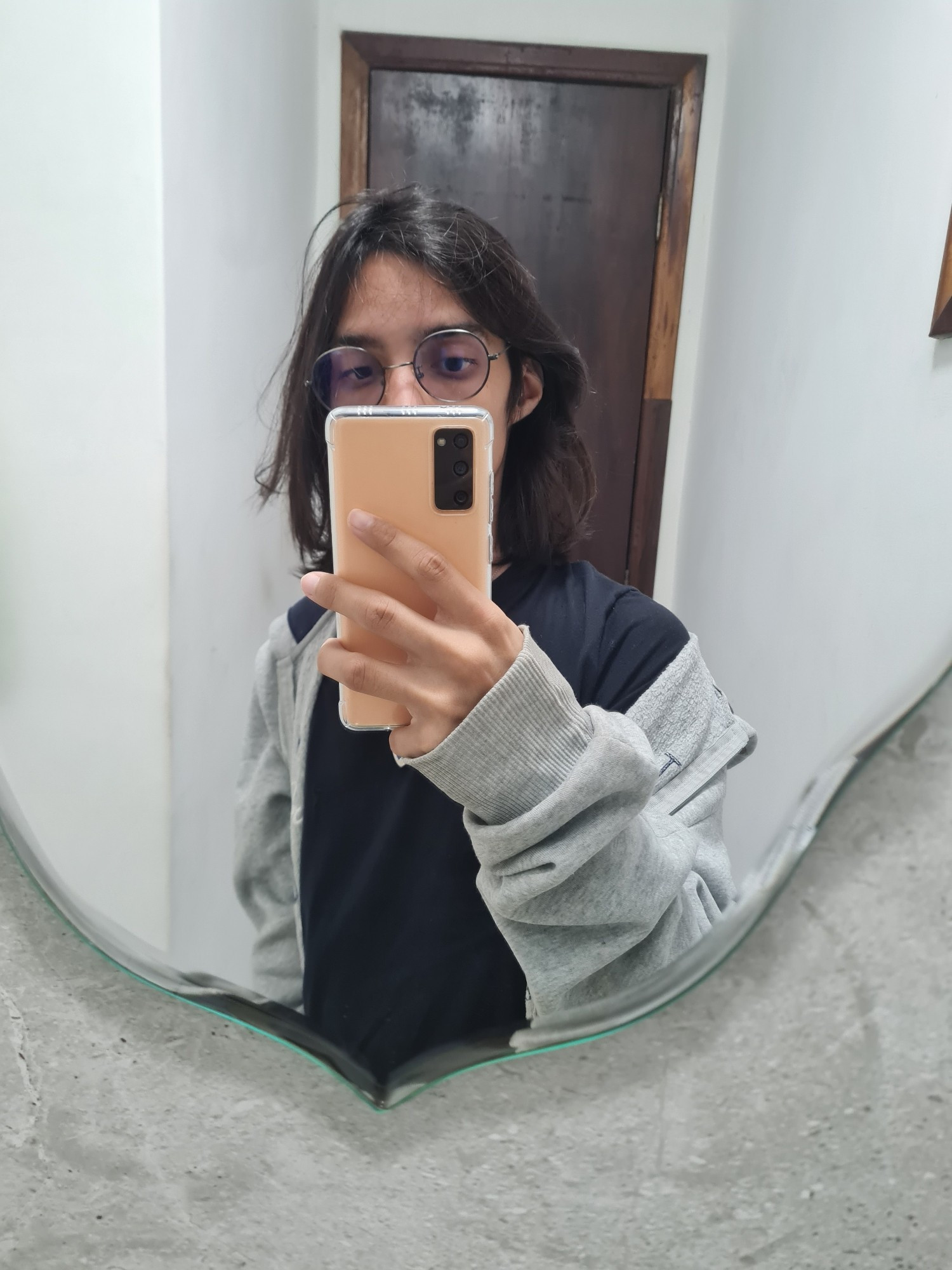 A taned medium haired girl using round glasses taking a pic at the bathroom's mirror.