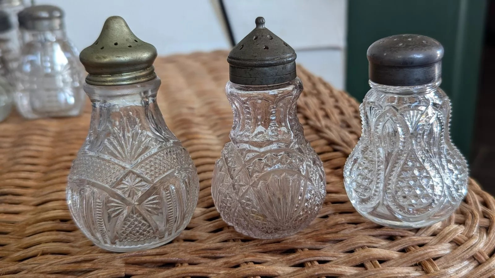 A set of three cut glass condiment shakers with metal caps.