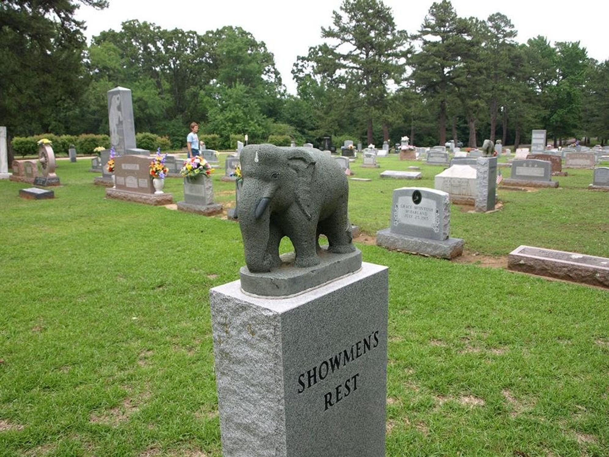 A plain, gray tombstone, stopped with a simplified elephant carving. The tombstone is inscribed with "Showmen's Rest."