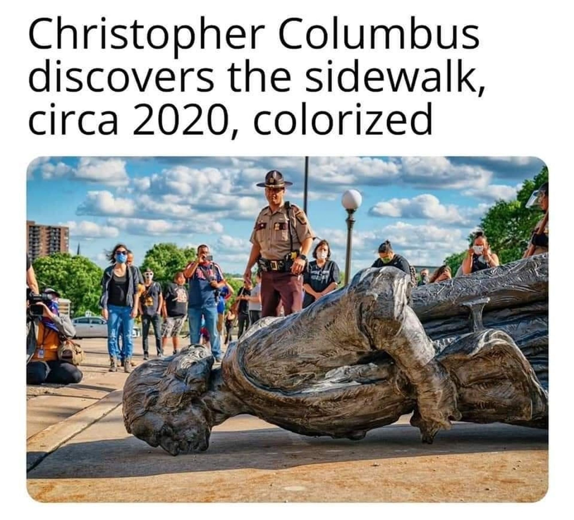 A picture of a statue of Christopher Columbus laying in the street with a caption of "Christopher Columbus discovers the sidewalk, circa 2020, colorized."