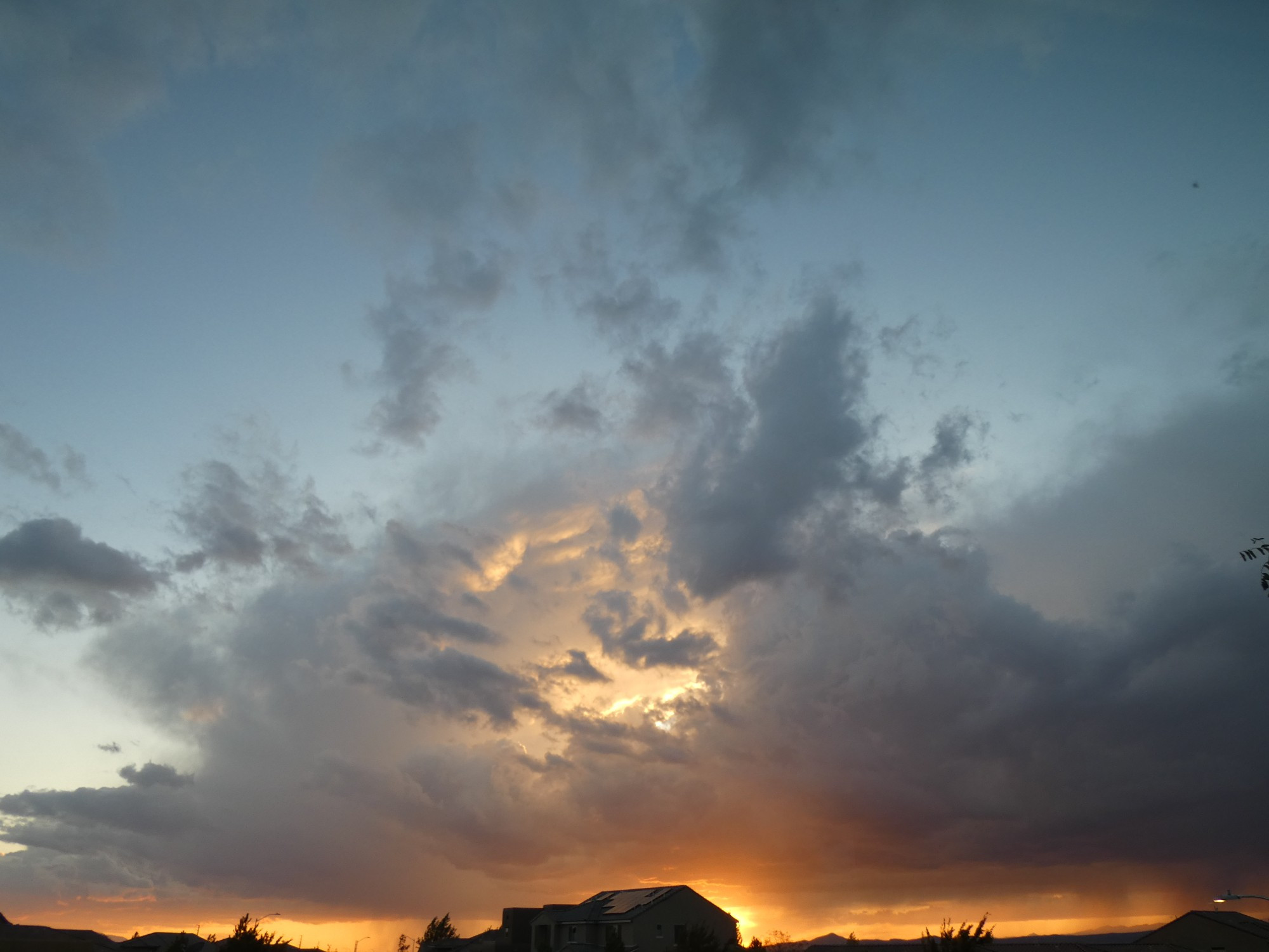 sunsetting, storm clouds are dark and grey, partially obscuring it, the sun is breaking through in the center  