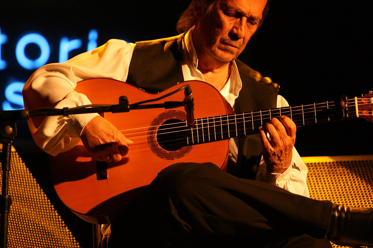 Paco de Lucía actuando en el Festival de jazz de Vitoria en el año 2010. Serio, mira hacia la guitarra con los ojos entre cerrados mientras viste con su tradicional camisa blanca y chaleco oscuro. Alberto Cabello • CC BY 2.0
