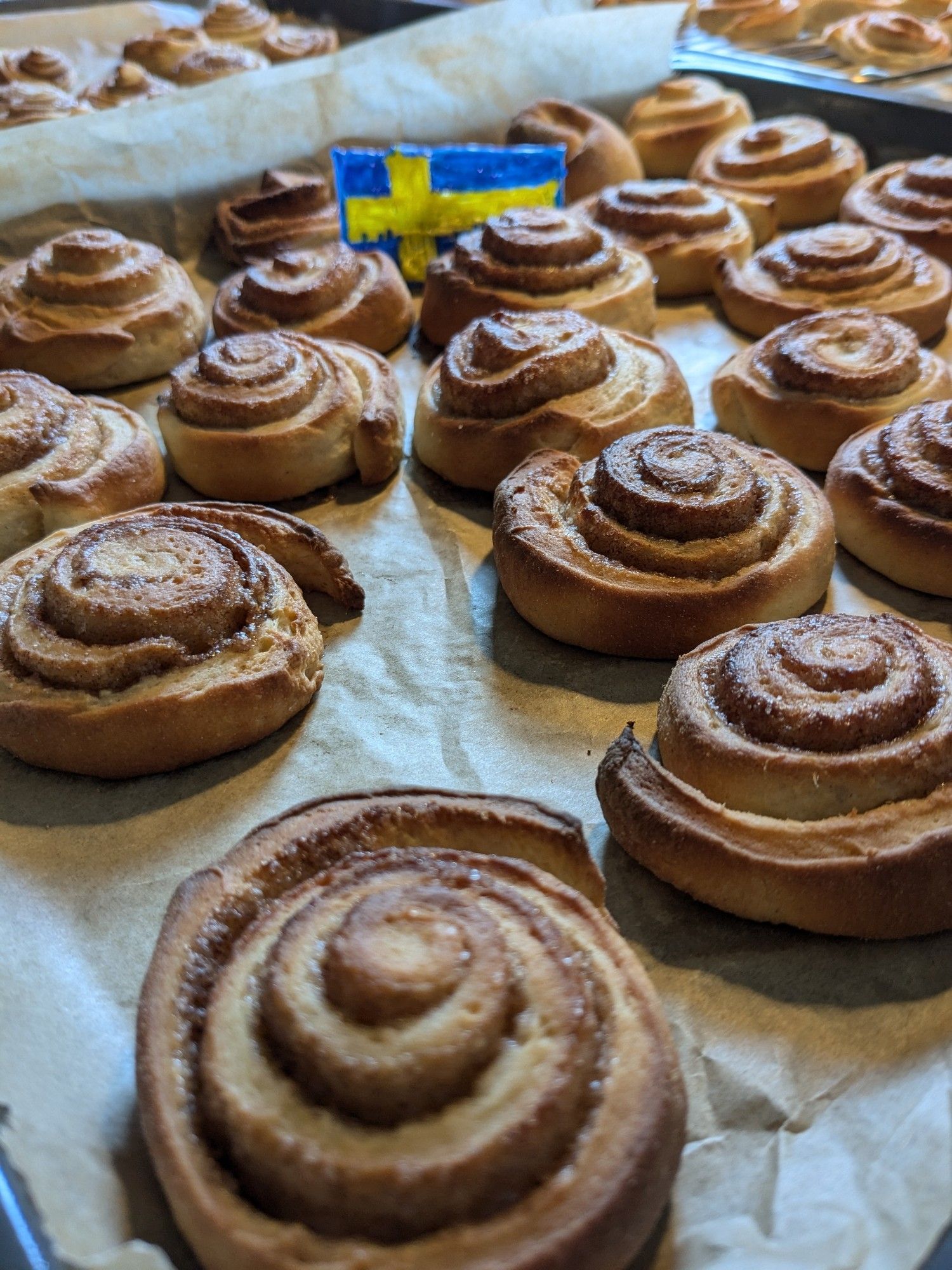 Schwedische Zimtröllchen auf einem Backblech, im Hintergrund eine gebastelte Schweden-Fahne