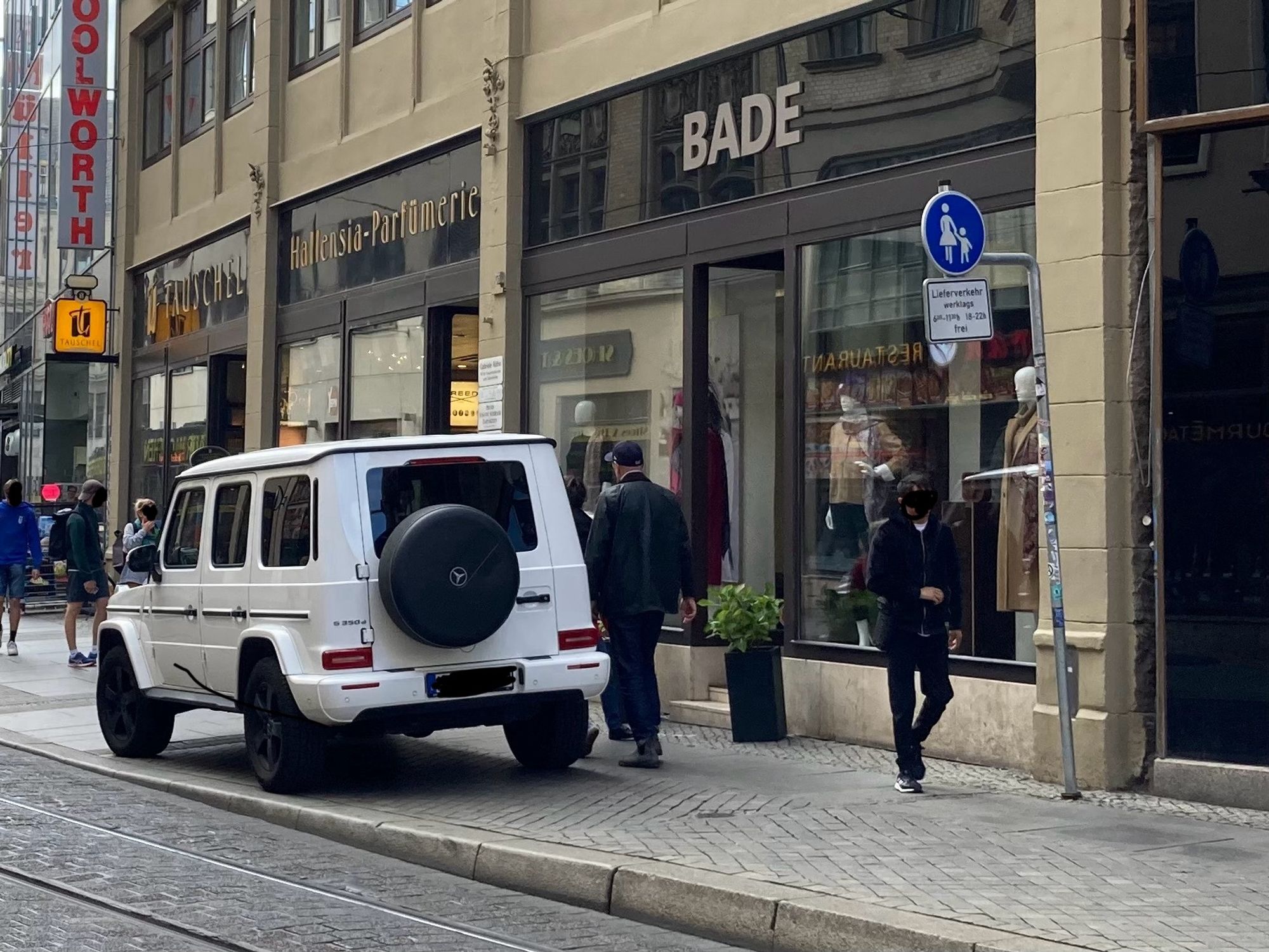 Ein weißer SUV steht auf einem Fußweg vor einem Ladengeschäft.