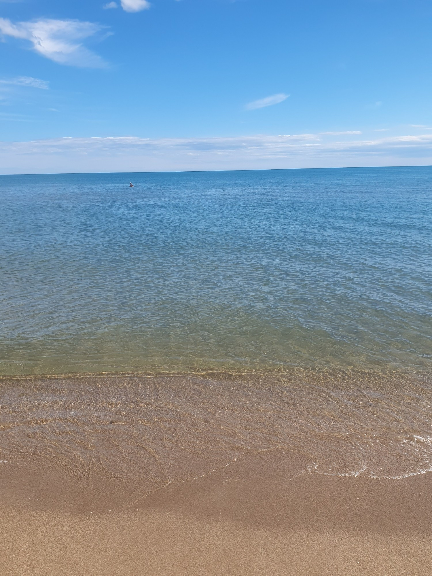 Ein glattes blaues Meer mit etwas Wolken am Horizont.