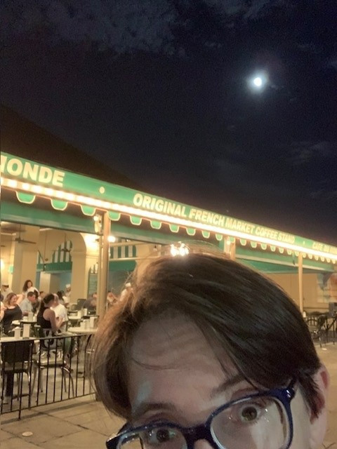 person (me) standing in front of Cafe Du Monde with moon in background