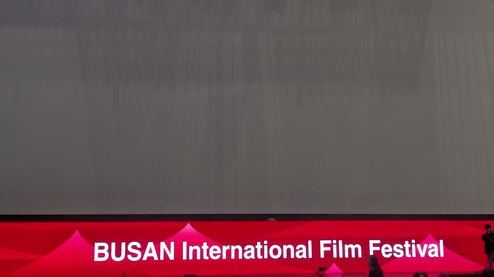 A large, blank movie screen with "BUSAN International Film Festival" in white on a red background below it