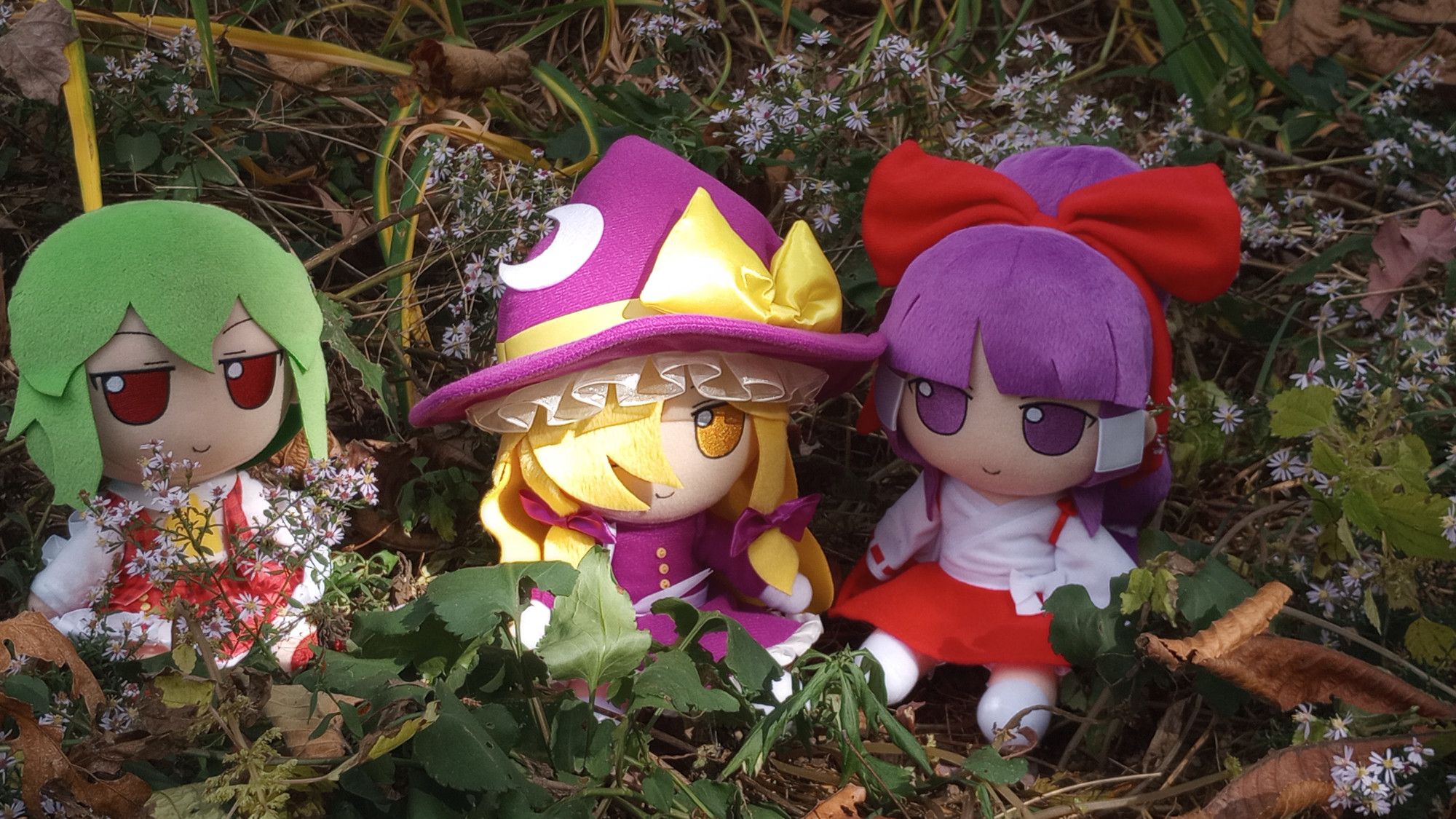 Yuuka fumo to the left, Classic Marisa fumo at the center with the sun shining on her, and Classic Reimu fumo on the right. They are surrounded by Blue Wood Asters and many other flora.