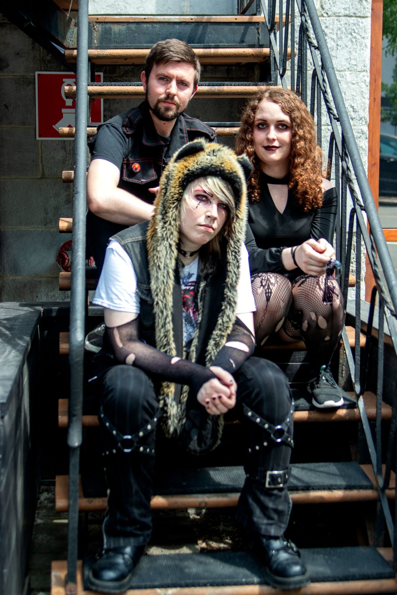 The current lineup of Anna Pest sitting on a staircase. Top left: Colin MacAndrew, drummer. Right: April Sada Solomon, bassist. Bottom left: April Hutchins, vocalist/guitarist/producer.