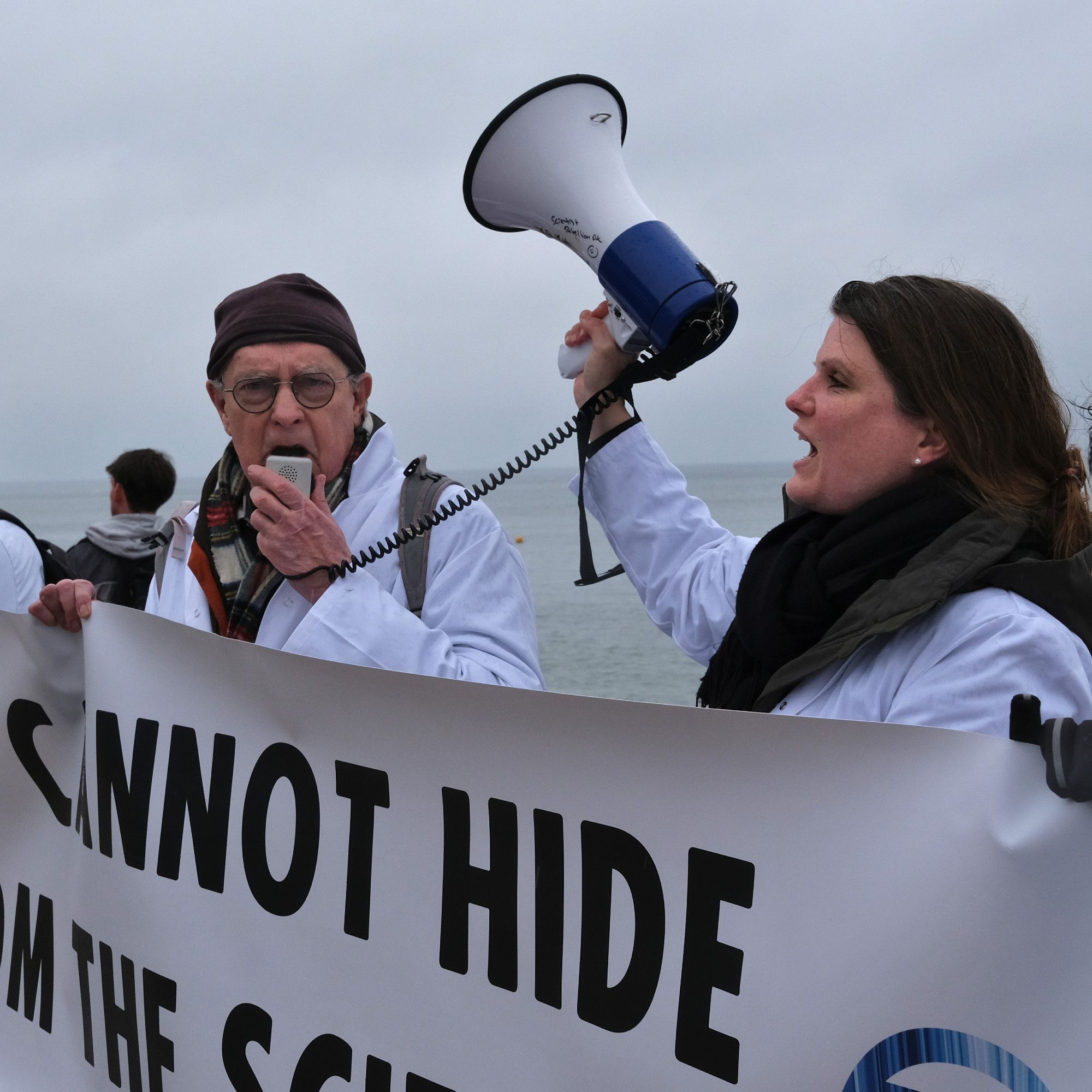 Two scientists holding a banner and speaking on a megaphone