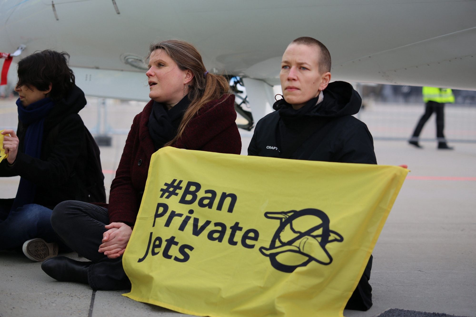 Scientist-activists sitting in front of a private jet at Aalborg, with a banner that reads "Ban Private Jets"