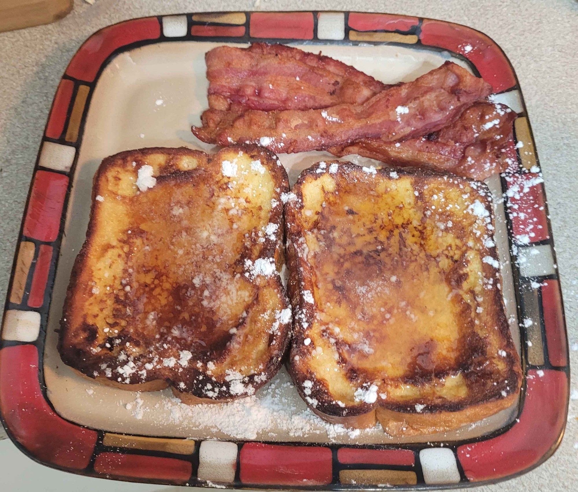 A picture of french toast and bacon on a square plate.