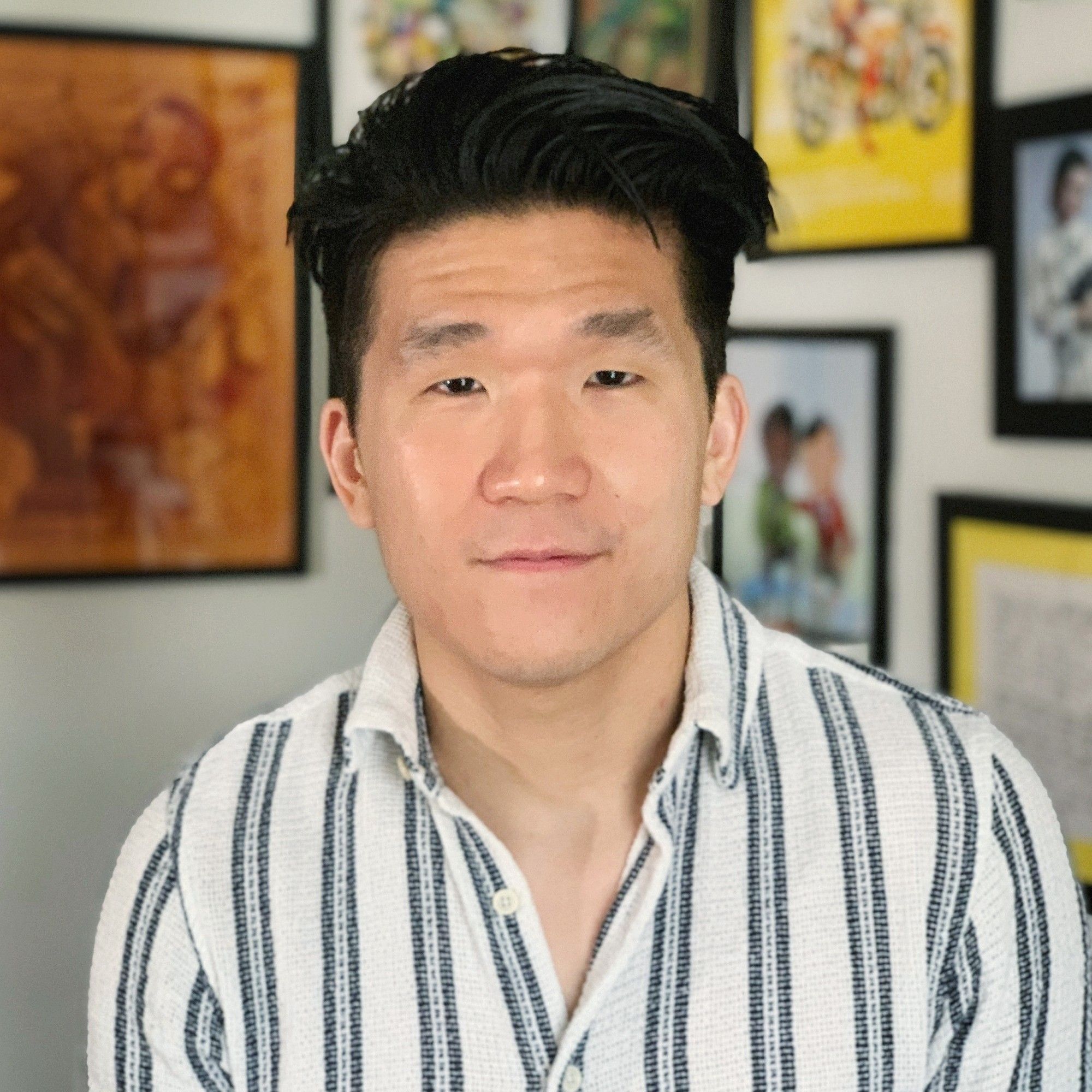 Headshot of myself. Wearing a vertical striped button down. Lots of nerdy parapheniela in the blurred background