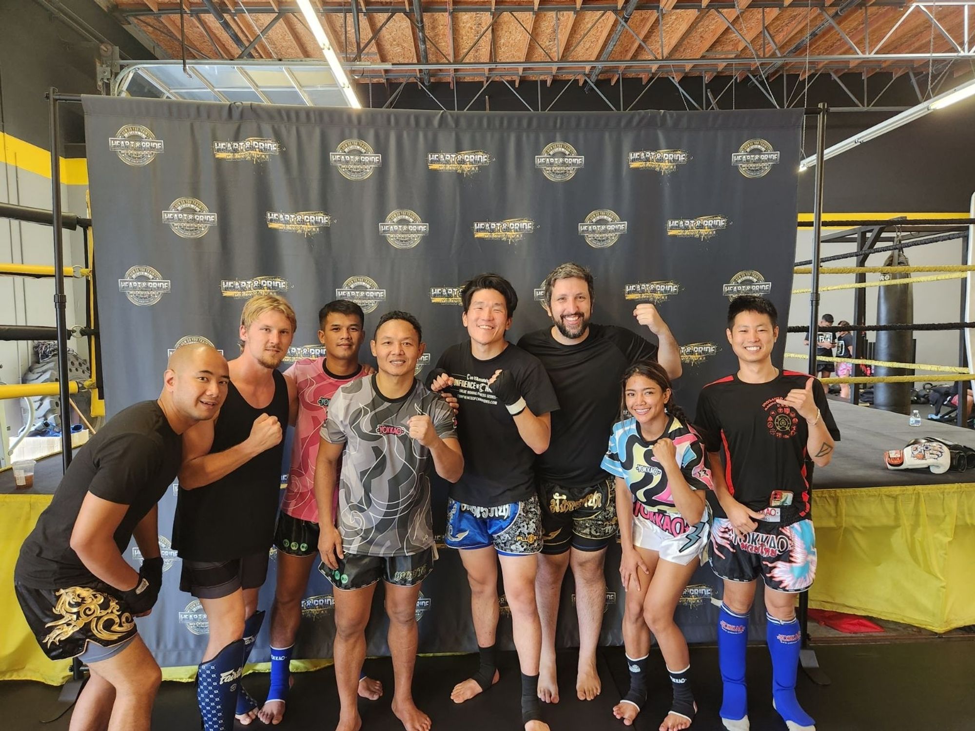 Photo of myself and some of my training partners alongside Saenchai + two other Muay Thai fighters. We're in front of a gym's step and repeat.