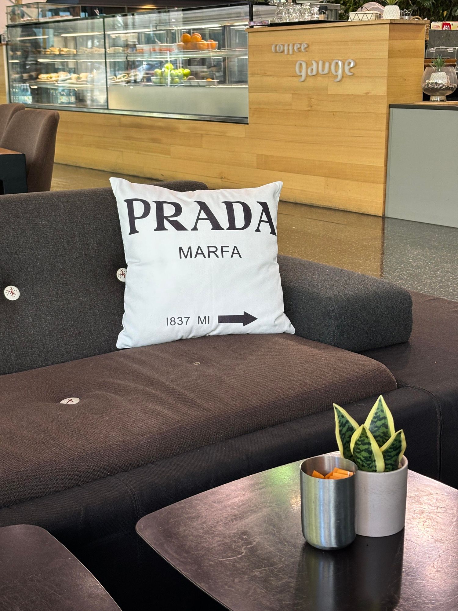 Cushion on a cafe sofa with lettering reading "Prada Marfa, 1837 miles".