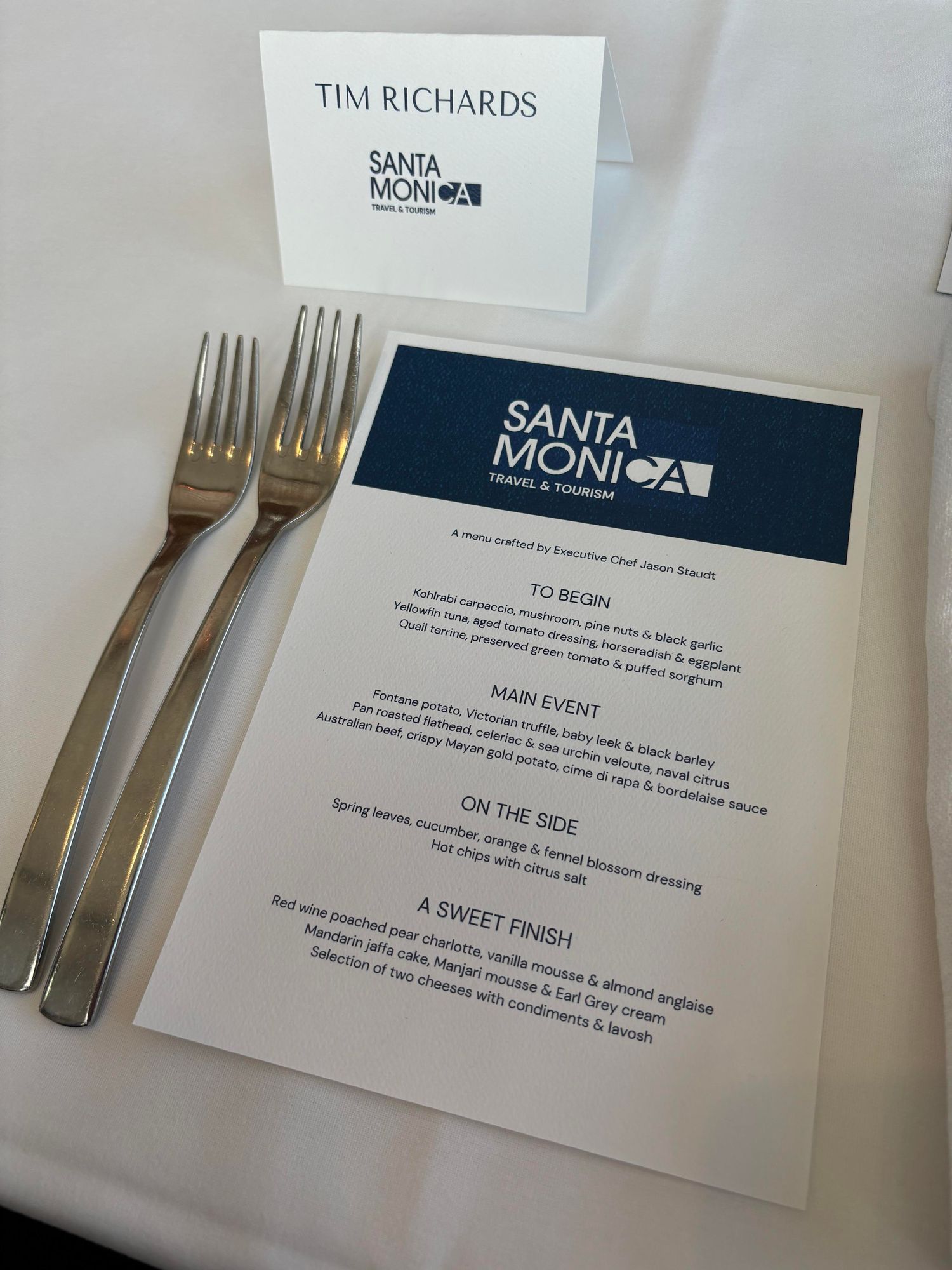 Menu and cutlery, on white tablecloth. 