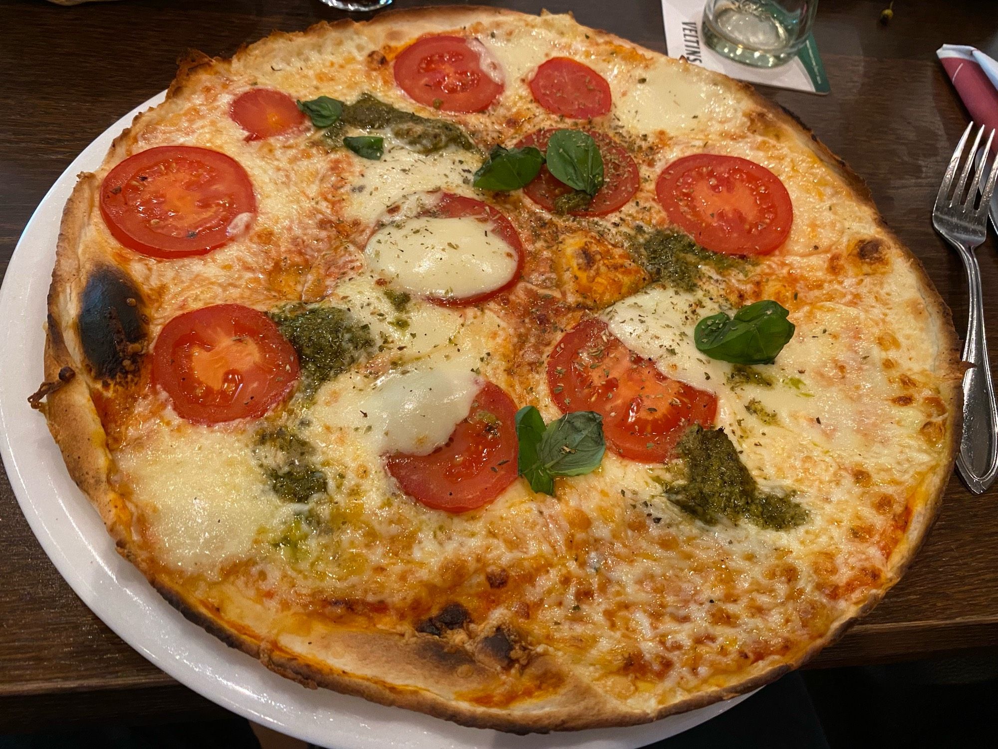 Pizza Caprese, with tomato slices, green pesto and basil leaves.