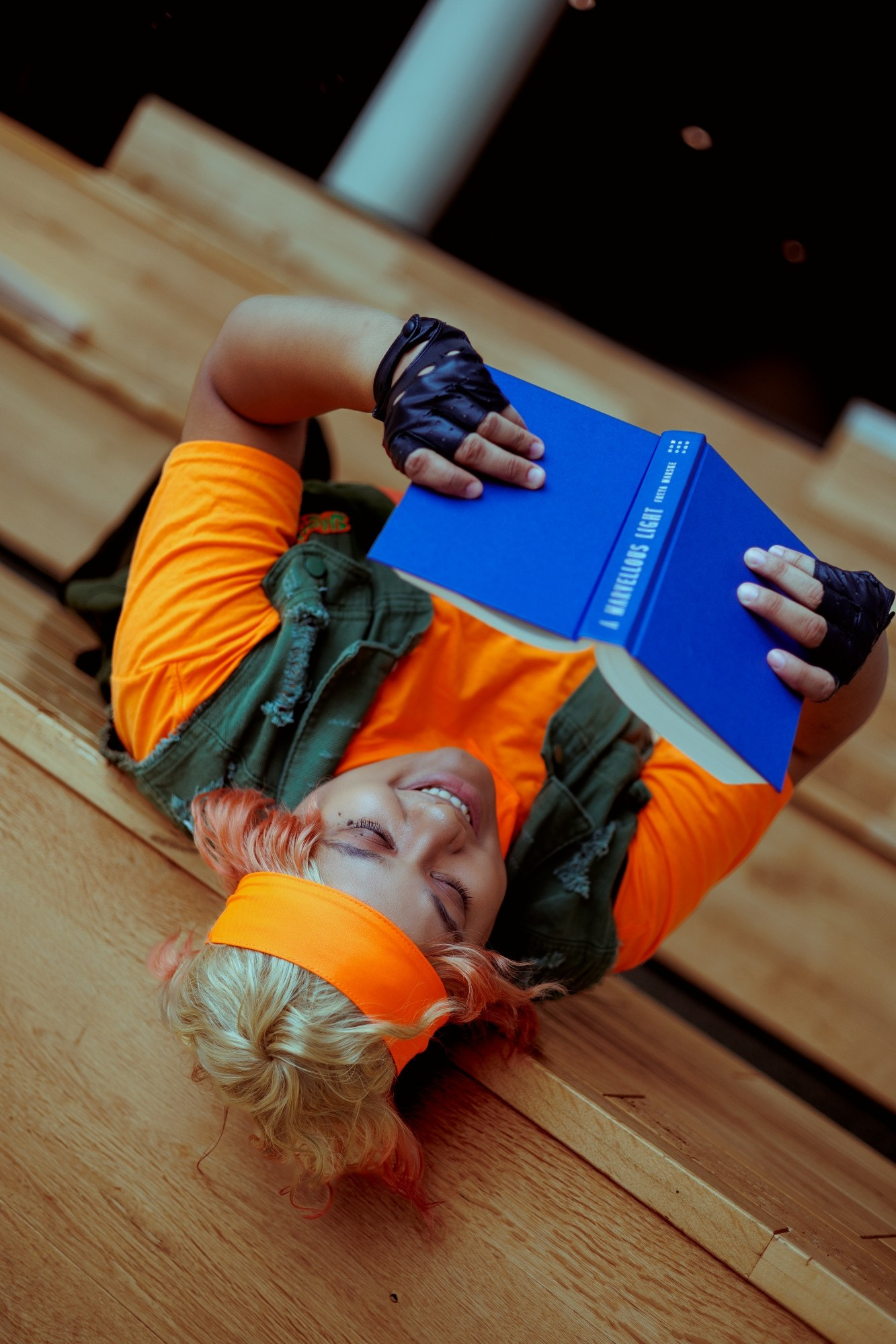 Nix dressed as Mikey from Teenage Mutant Ninja Turtles. They are laying upside down on a large step and reading a book. They have a smile on their face.