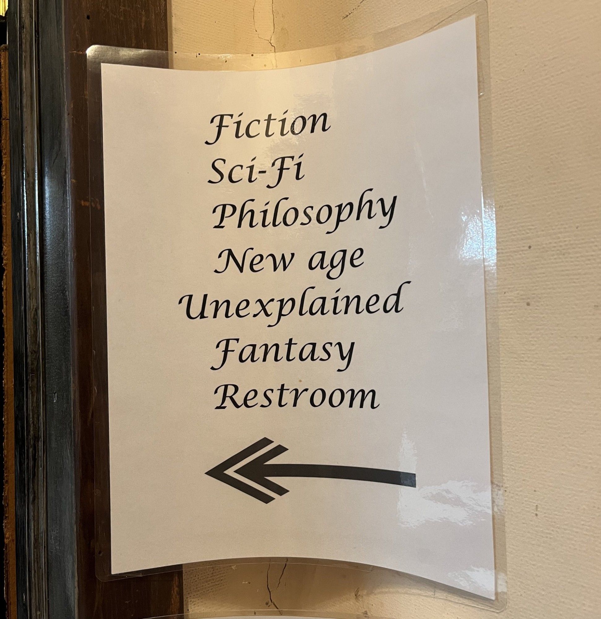 A sign says,
Fiction
Sci-Fi
Philosophy
New age
Unexplained
Fantasy
Restroom