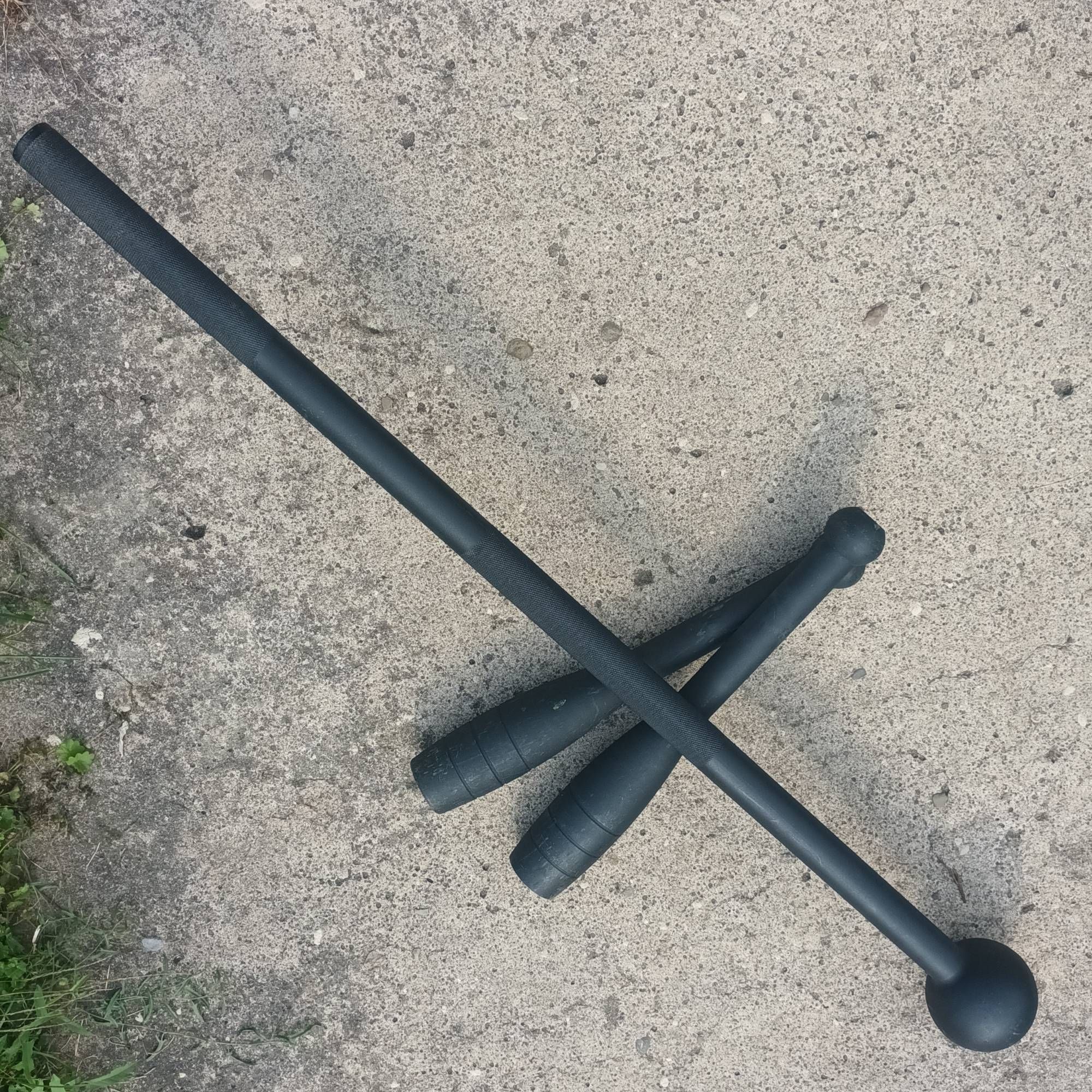 A 10lbs black steel mace laying across two 10lbs black club bells on concrete