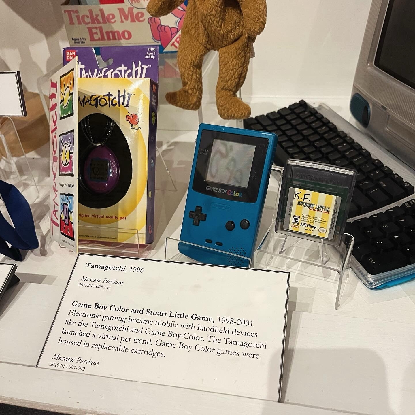 Photo from museum exhibit showing a game boy color and tamagotchi.