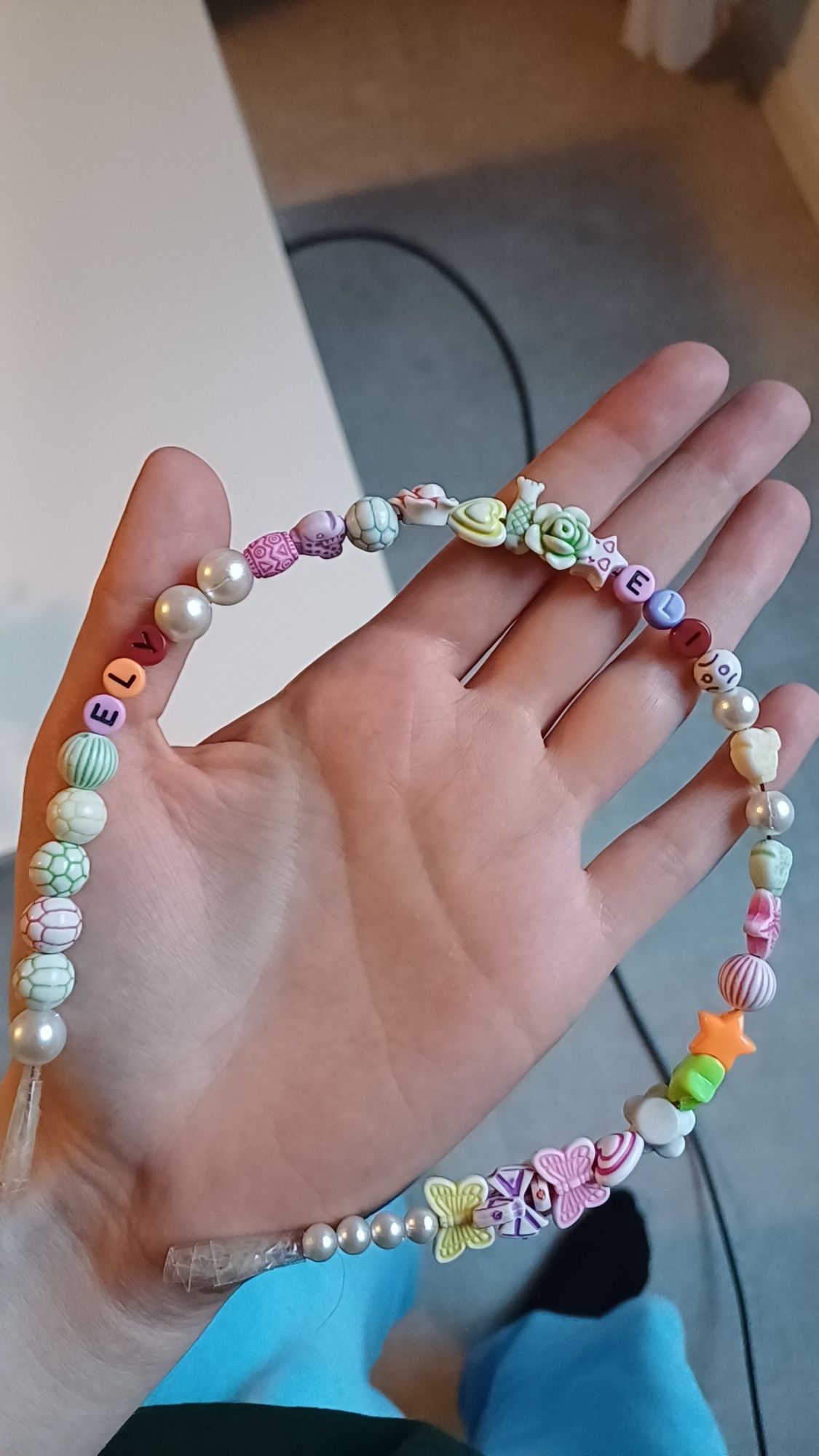 photo of a hair band made by a kid of a bunch of different beads including some with letters on them that spell "ELY" and "ELI"