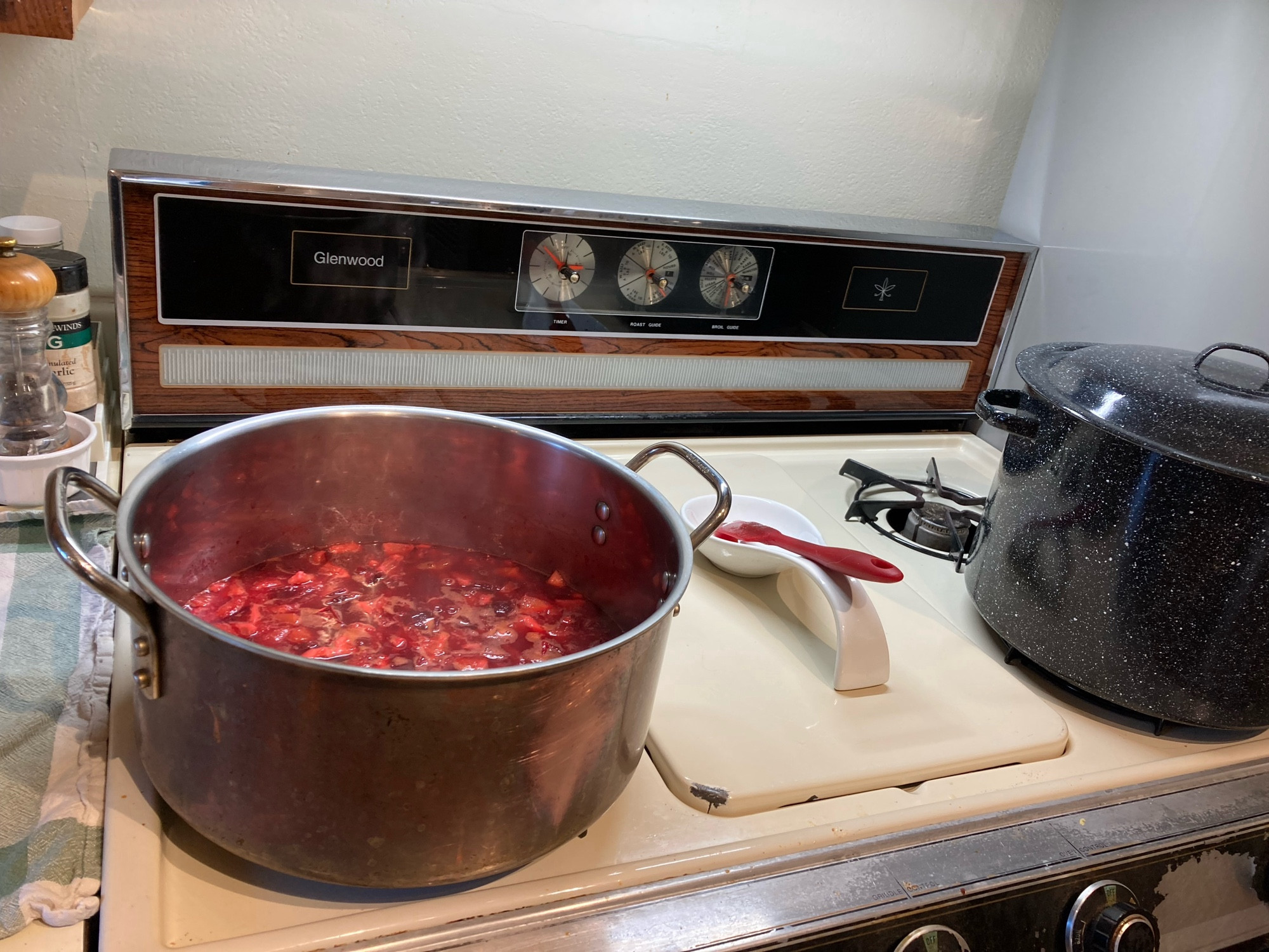 Plum and lemons cooking in a pot on a stove next to a canning kettle