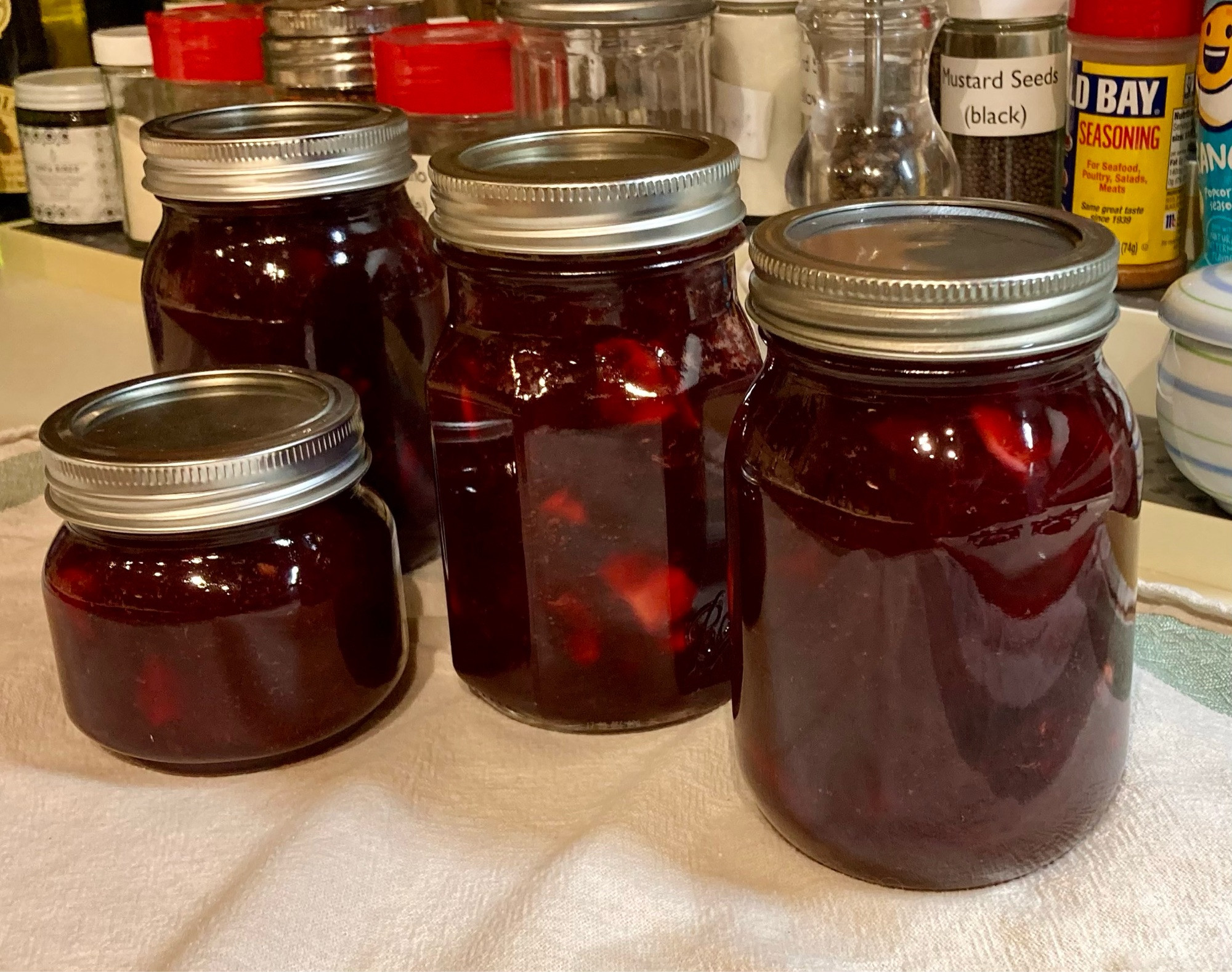 Four jars of jam on a towel on a counter with spices in the background.