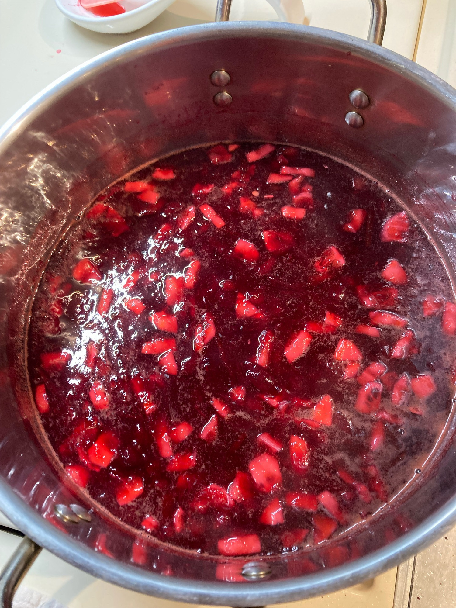 Jam is dark and glossy with sugar as it cooks in a pot