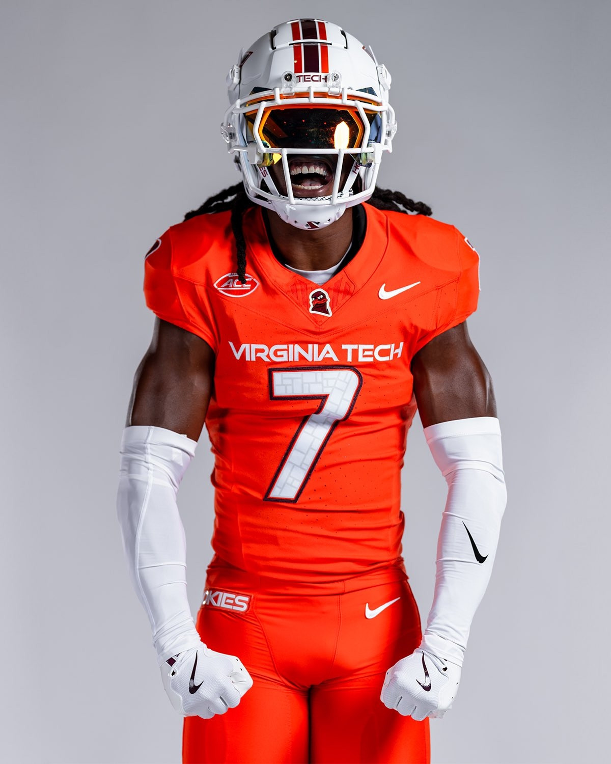 A Virginia Tech Hokie football player flexing, wearing all orange pants and jersey. 