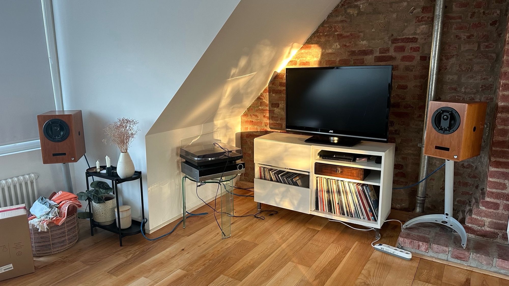 A corner in an attic apartment with a sideboard and a TV in front of a brick wall.