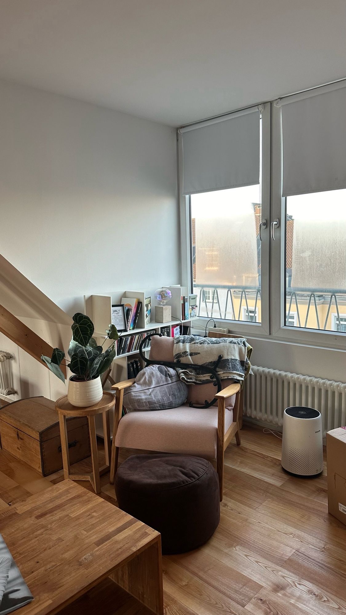 A corner in a attic apartment with a White bookshelf and a cozy armchair with a blanke, a deathstar pillow and a footrest.