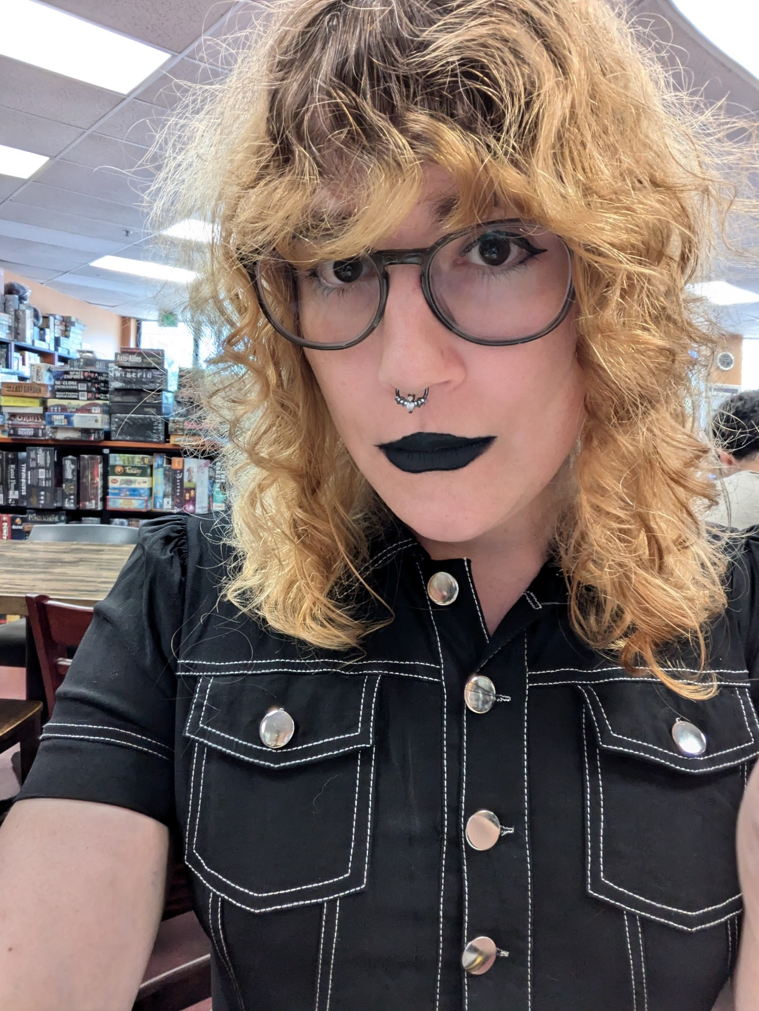 Trans girl with strawberry blonde hair wearing a black romper with white outline and glasses with black makeup on