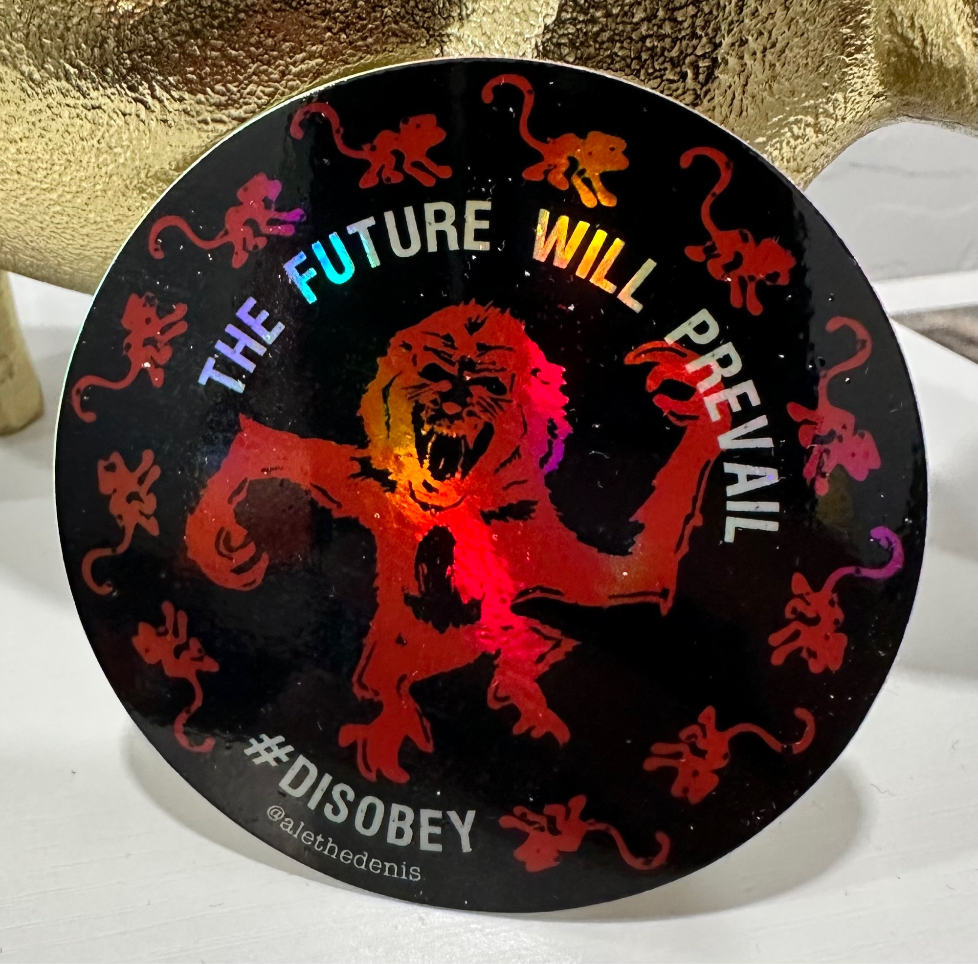 The army of the 12 monkeys logo inspired sticker in red with transparent text that reads “THE FUTURE WILL PREVAIL” and hashtag Disobey 